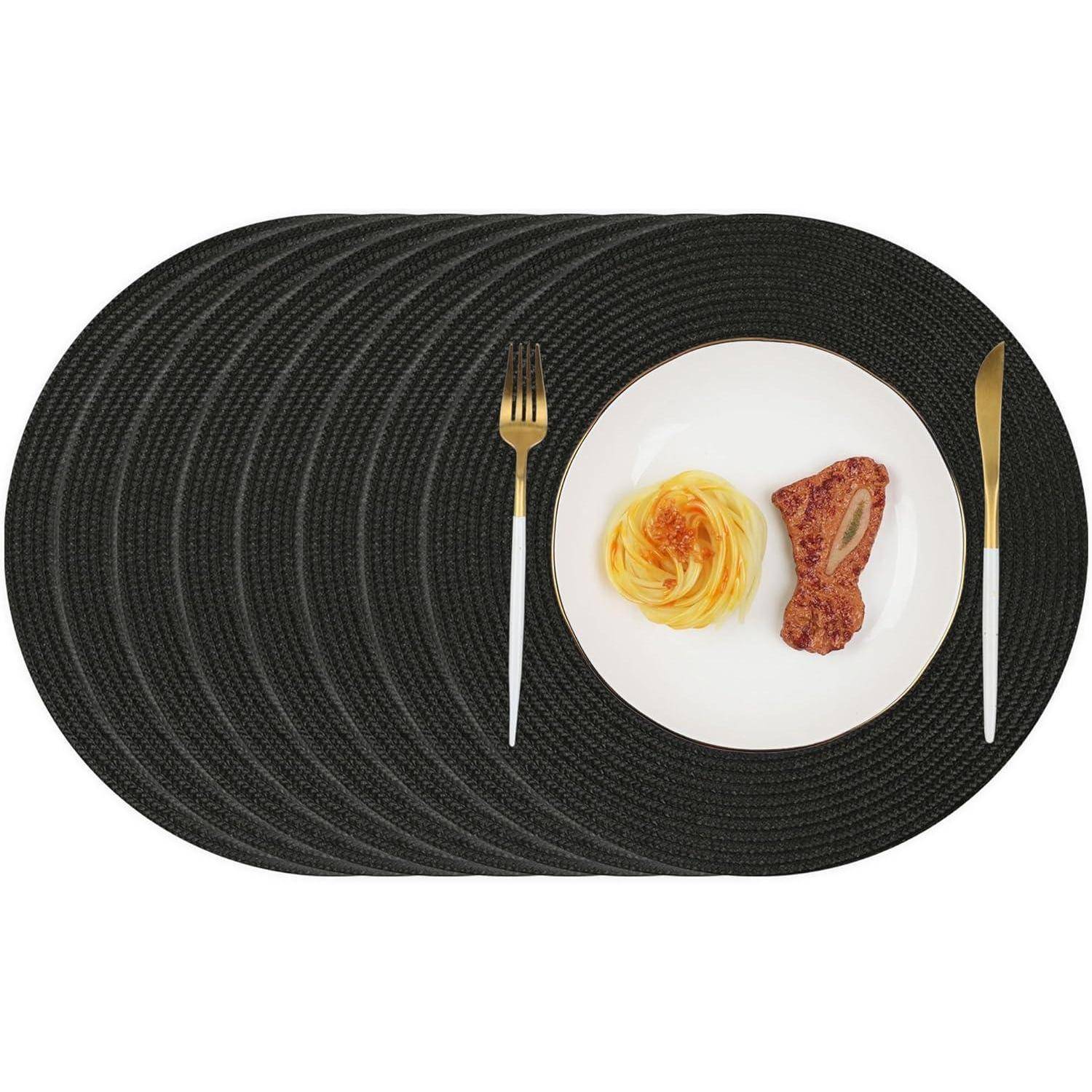 Ein schwarzes ovales Platzdeckchen mit einem weißen Teller, der eine Nudelwendel und ein Steak enthält. Eine Gabel und ein Messer sind links und rechts neben dem Teller platziert.