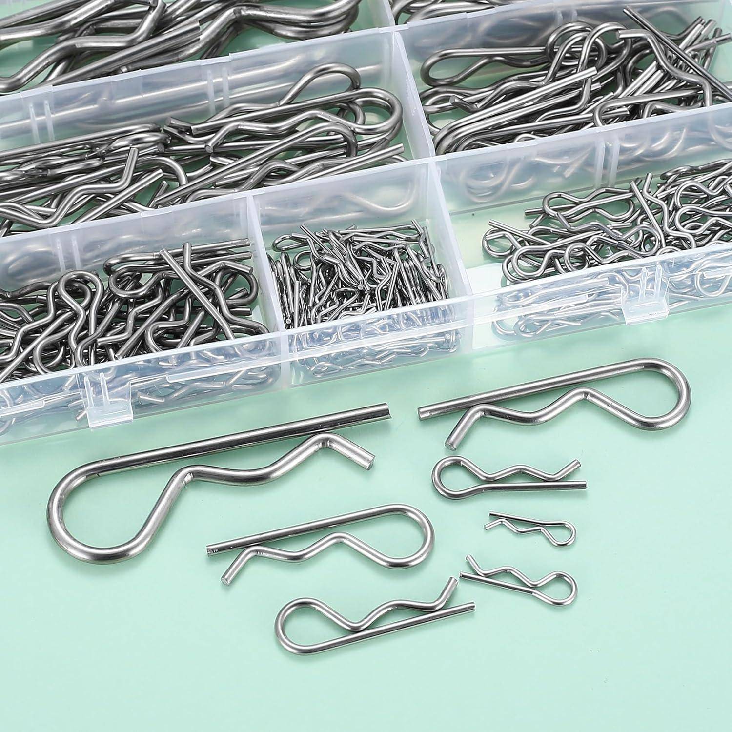 Sammlung von silbernen Metallstiften in verschiedenen Größen, organisiert in einer fächerigen Kunststoffbox auf einer grünen Oberfläche.