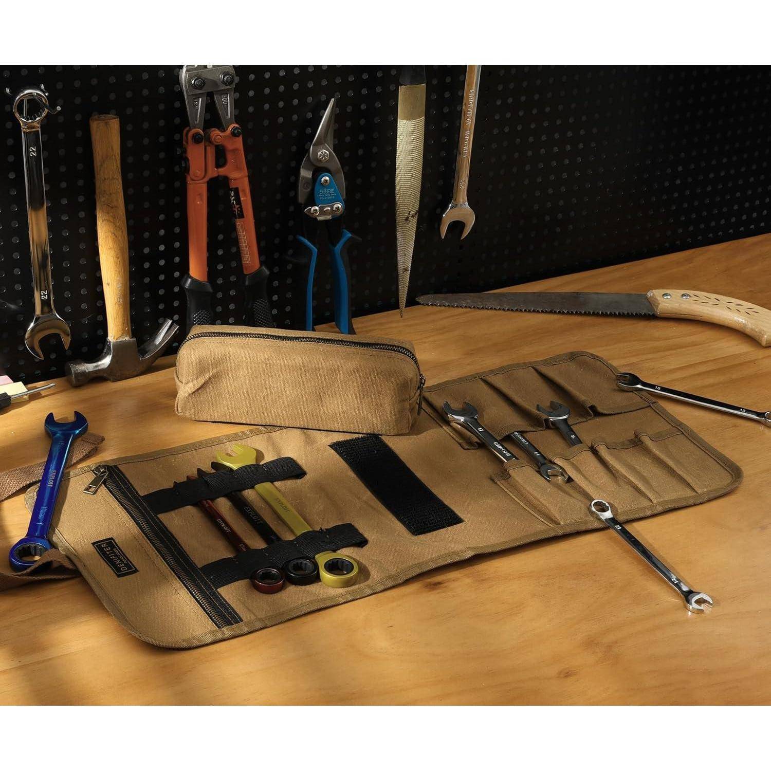 Eine Werkzeugtasche ist auf einem Holztisch ausgerollt und zeigt verschiedene Werkzeuge wie einen Schraubenschlüssel, Schraubendreher und Zangen. Weitere Werkzeuge hängen an einer Werkzeugwand mit Löchern.