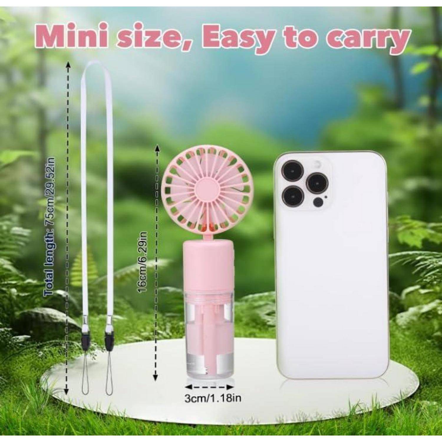Kompakt in Größe, Leicht zu tragen - rosa Ventilator und ein Smartphone auf Gras, der die kompakte Größe des Ventilators hervorhebt: 16 cm Höhe, 3 cm Durchmesser, mit Trageriemen.