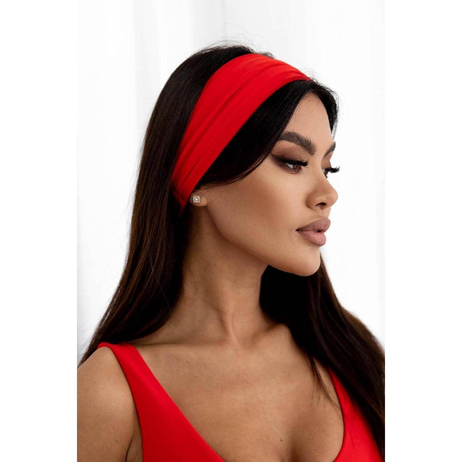 Eine Person mit langen dunklen Haaren, die ein rotes Stirnband und ein rotes Oberteil trägt, blickt seitlich vor einem hellen Hintergrund.