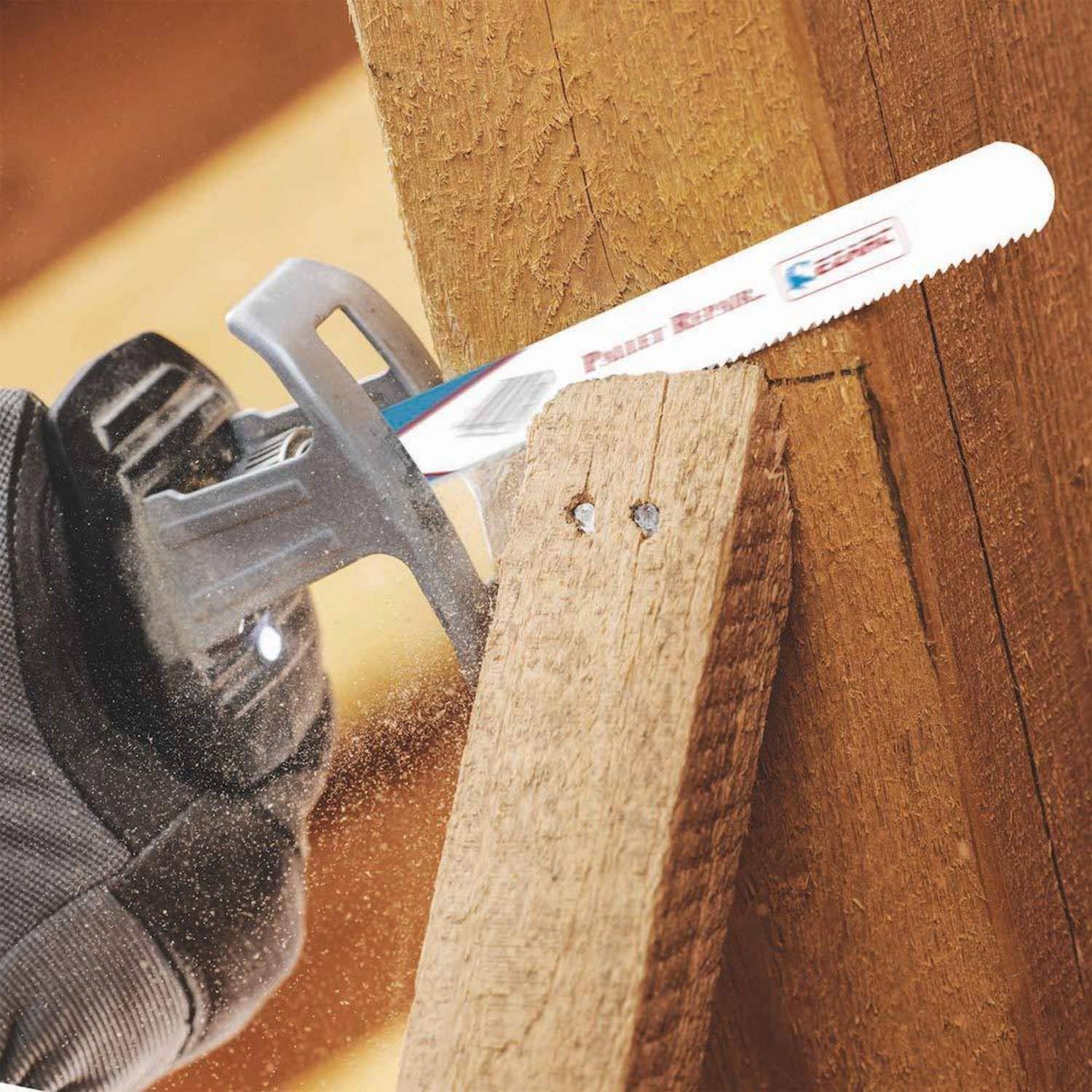 Eine Person, die eine Stichsäge verwendet, um durch eine Holzplanke zu schneiden. Sägespäne sind sichtbar, was auf aktives Sägen hinweist.