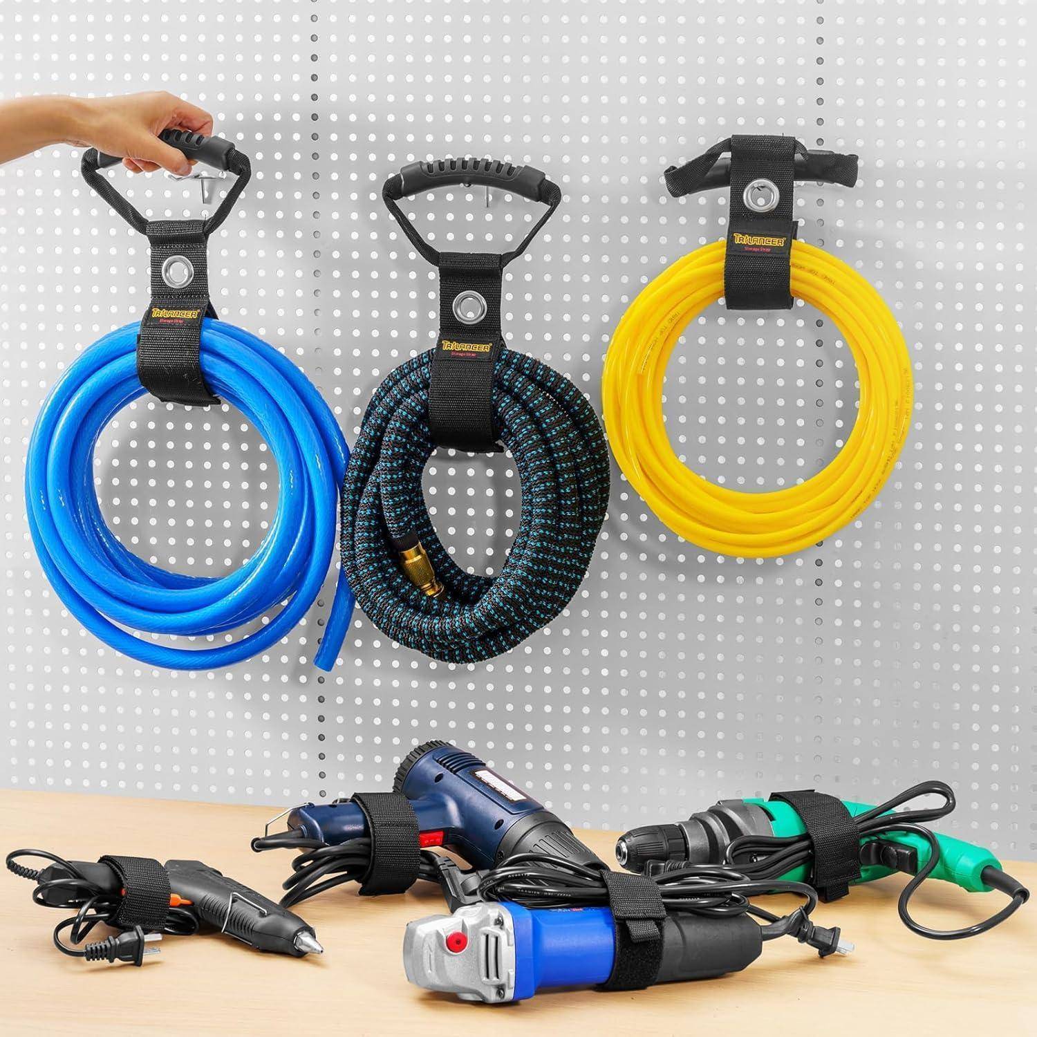 Drei einziehbare Haken an einer Wand halten sicher blaue, schwarze und gelbe Seile. Darunter sind verschiedene aufgerollte Kabel und Werkzeuge ordentlich angeordnet.