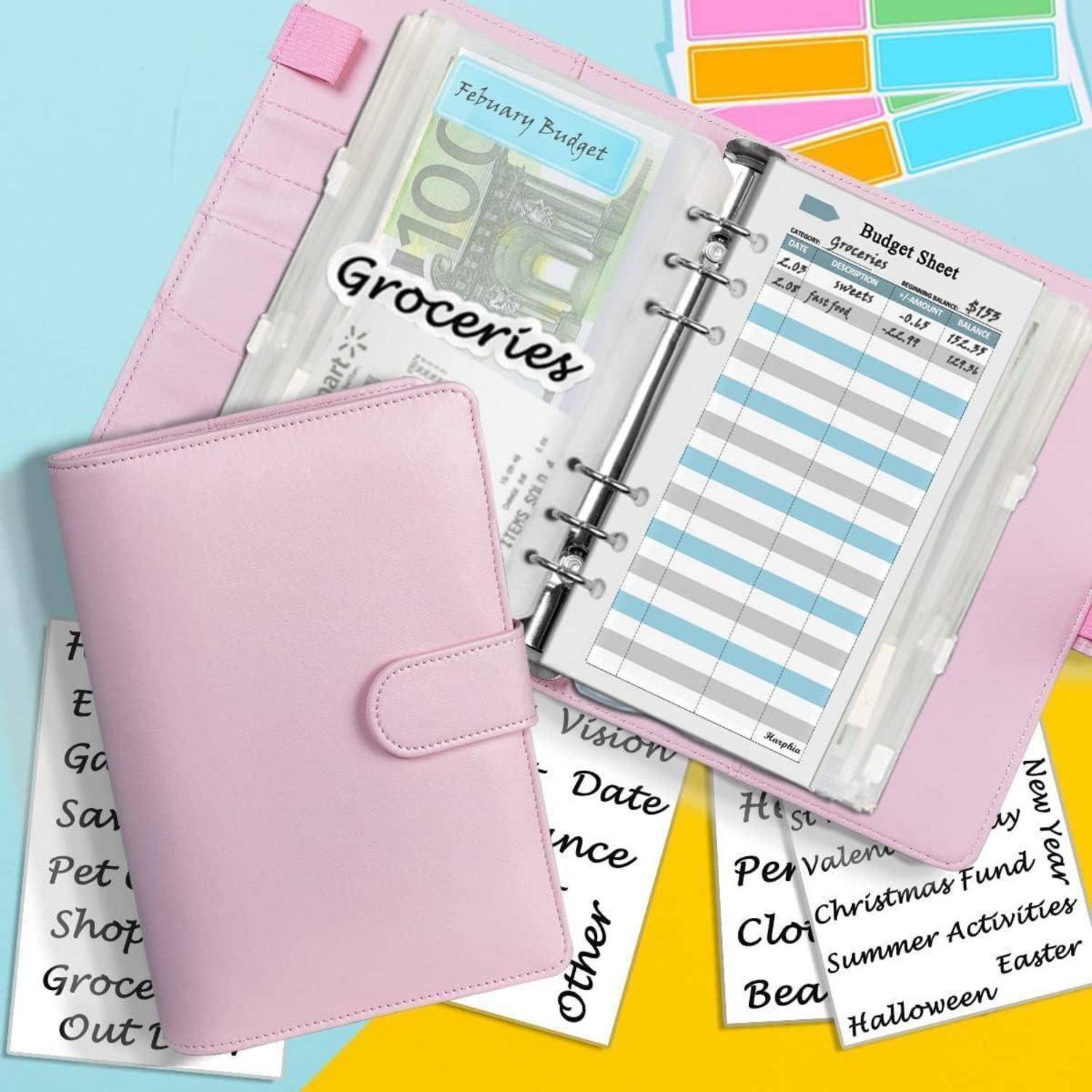 Ein rosa Planer, der auf einer Budgetliste für Lebensmittel geöffnet ist und Euro-Währung zeigt. Haftnotizen und beschriftete Umschläge für monatliche Ausgaben umgeben ihn.
