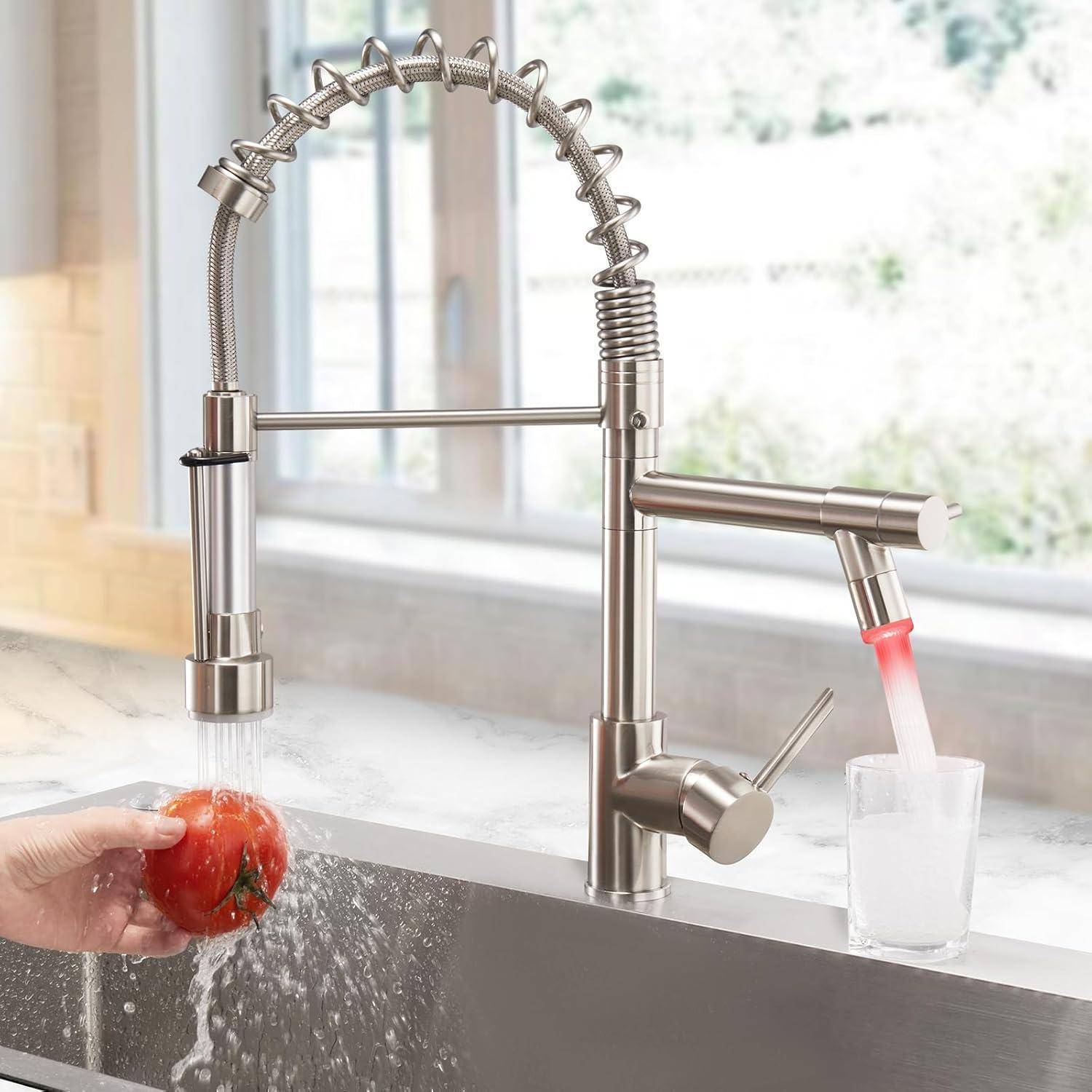 Ein moderner Küchenarmatur spritzt Wasser über eine Tomate, die über dem Spülbecken gehalten wird. Ein weiterer Wasserstrahl füllt ein Glas auf der Arbeitsplatte.