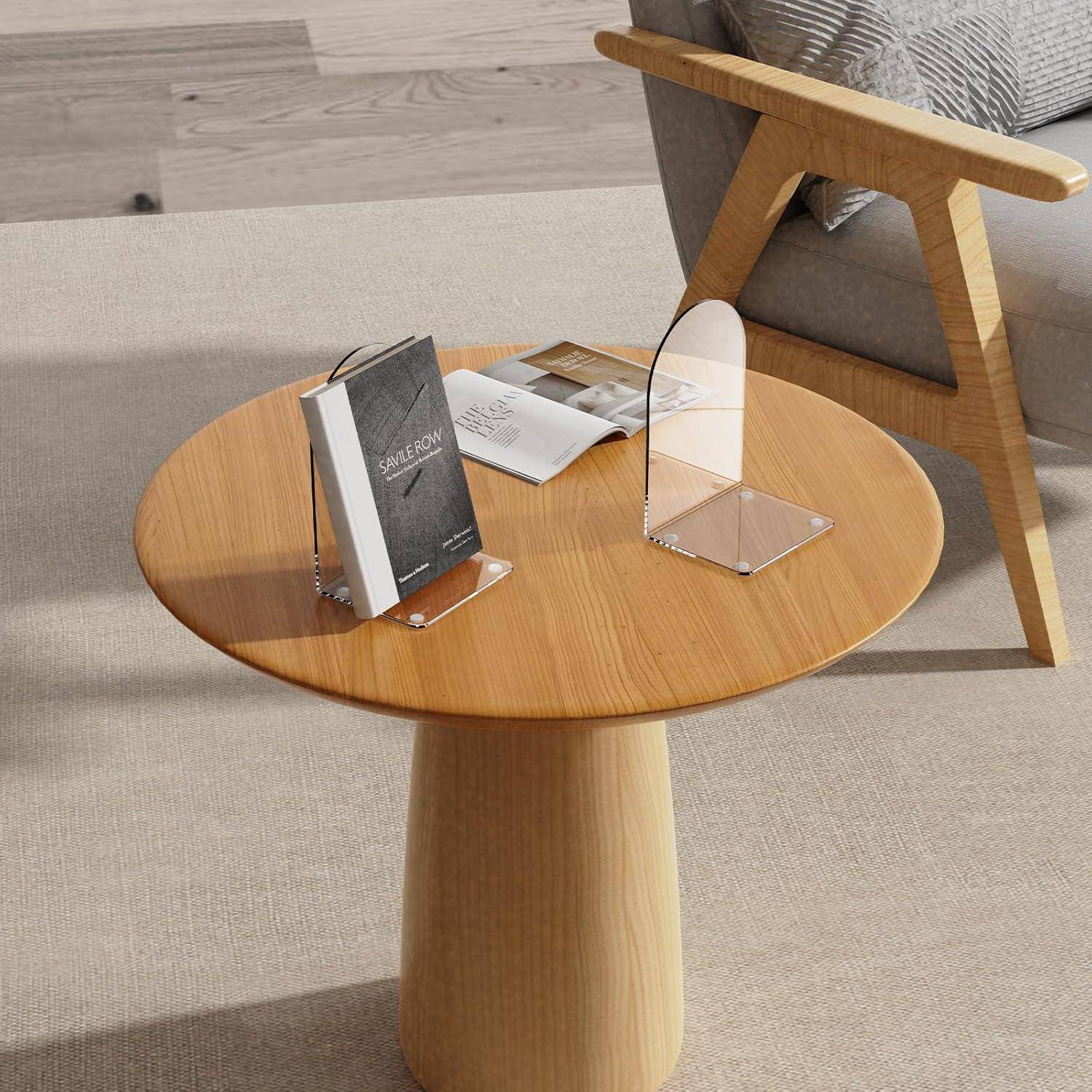 Ein runder Holztisch mit Büchern und einem transparenten Dekorationsobjekt steht neben einem gepolsterten Stuhl auf einem hellgefärbten Teppichboden.