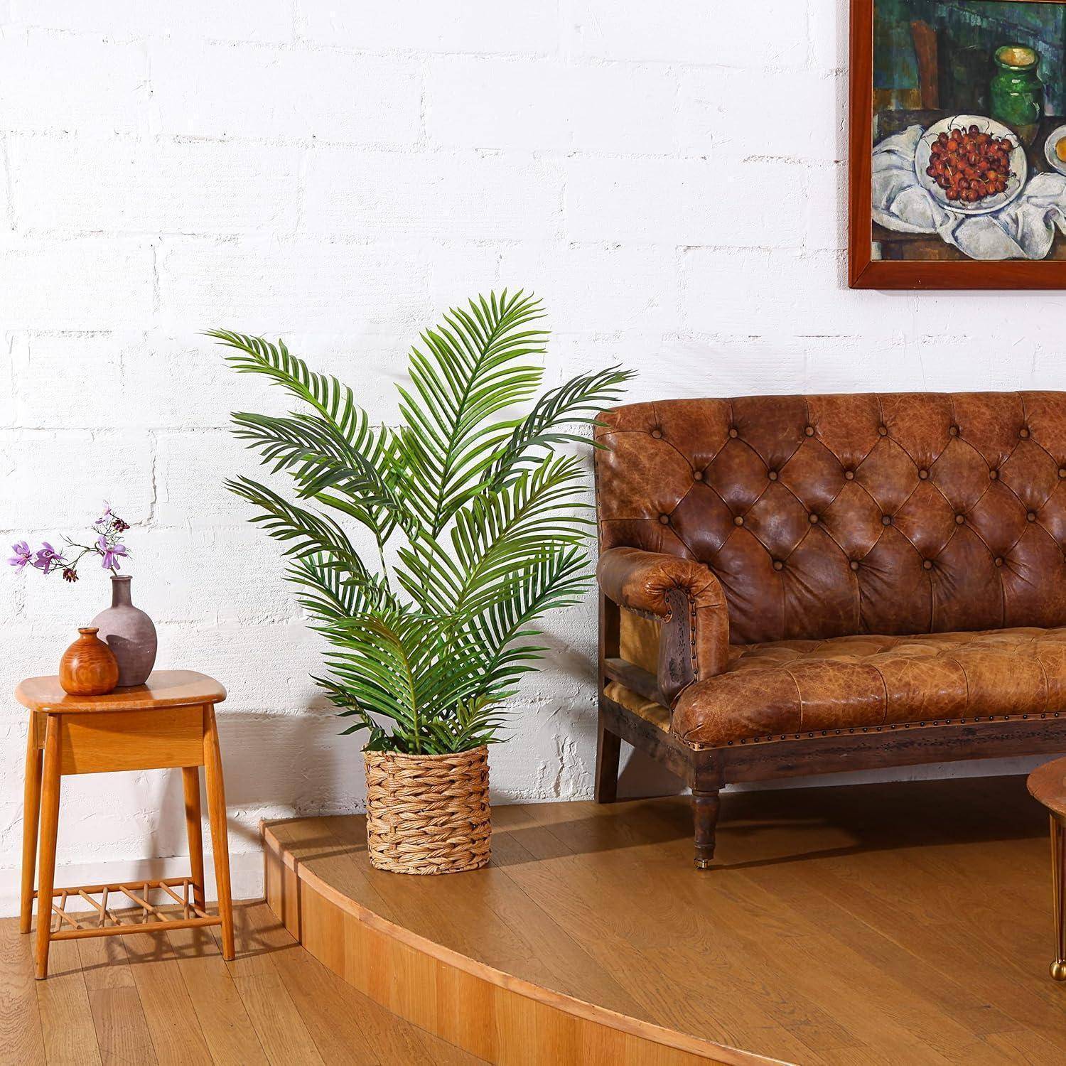 Ein Vintage-Ledersofa auf einer Holzplattform, daneben eine Zimmerpflanze. In der Nähe steht ein kleiner Holztisch mit einer Vase und Dekoration, vor einer weißen Wand.