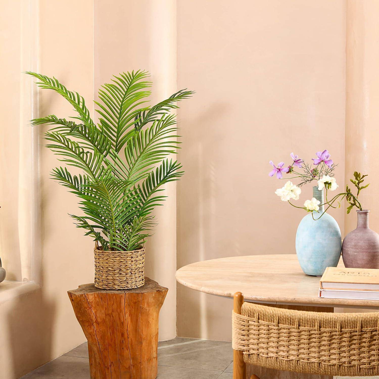 Ein kleiner runder Tisch mit einer blauen Vase, die weiße und lila Blumen enthält, steht neben einem Korbstuhl. Eine Topfpflanze sitzt auf einem Holzhocker.