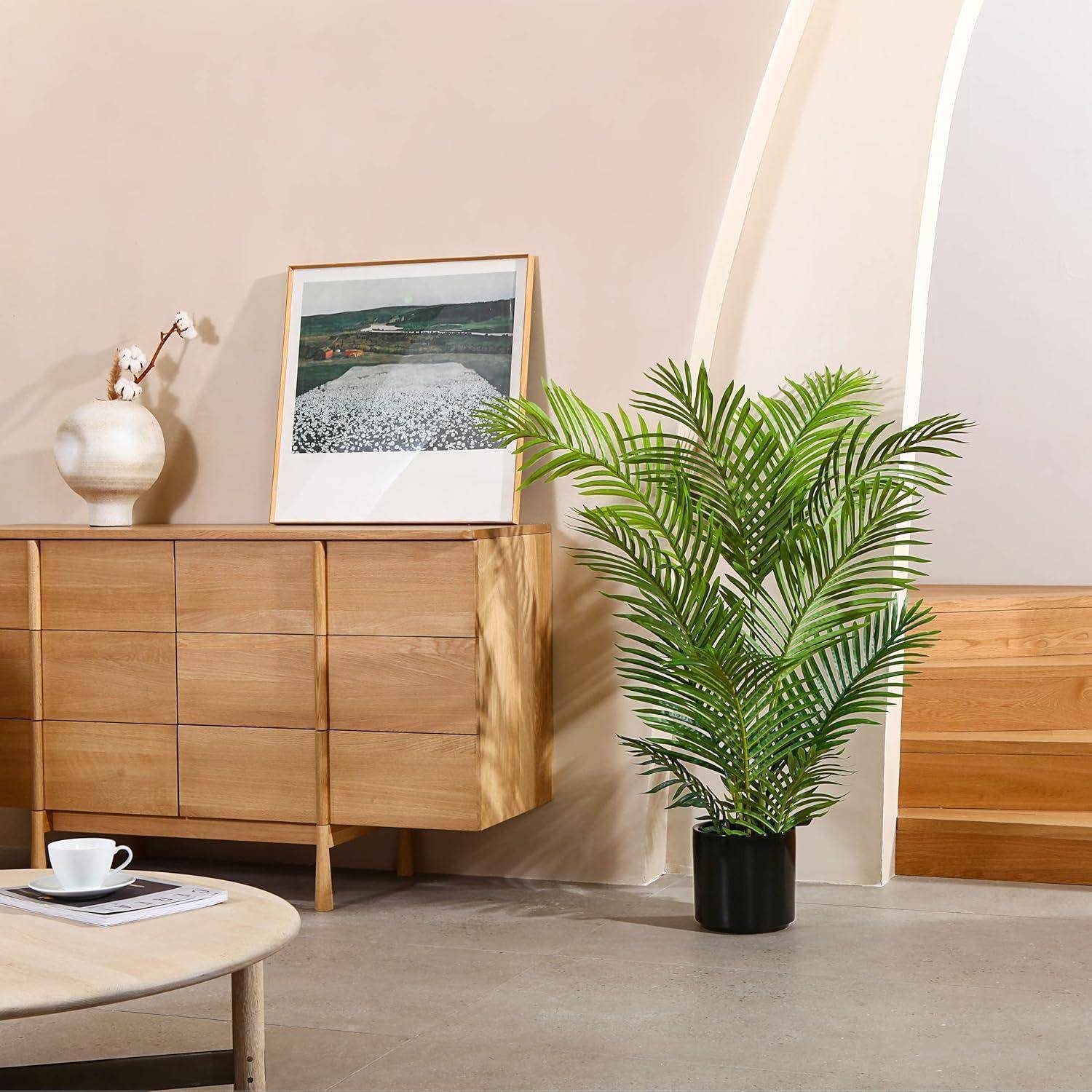 Ein moderner Wohnraum zeigt ein Holzsideboard mit einem gerahmten Landschaftsfoto, einer weißen Vase und einer großen Topfpflanze daneben.