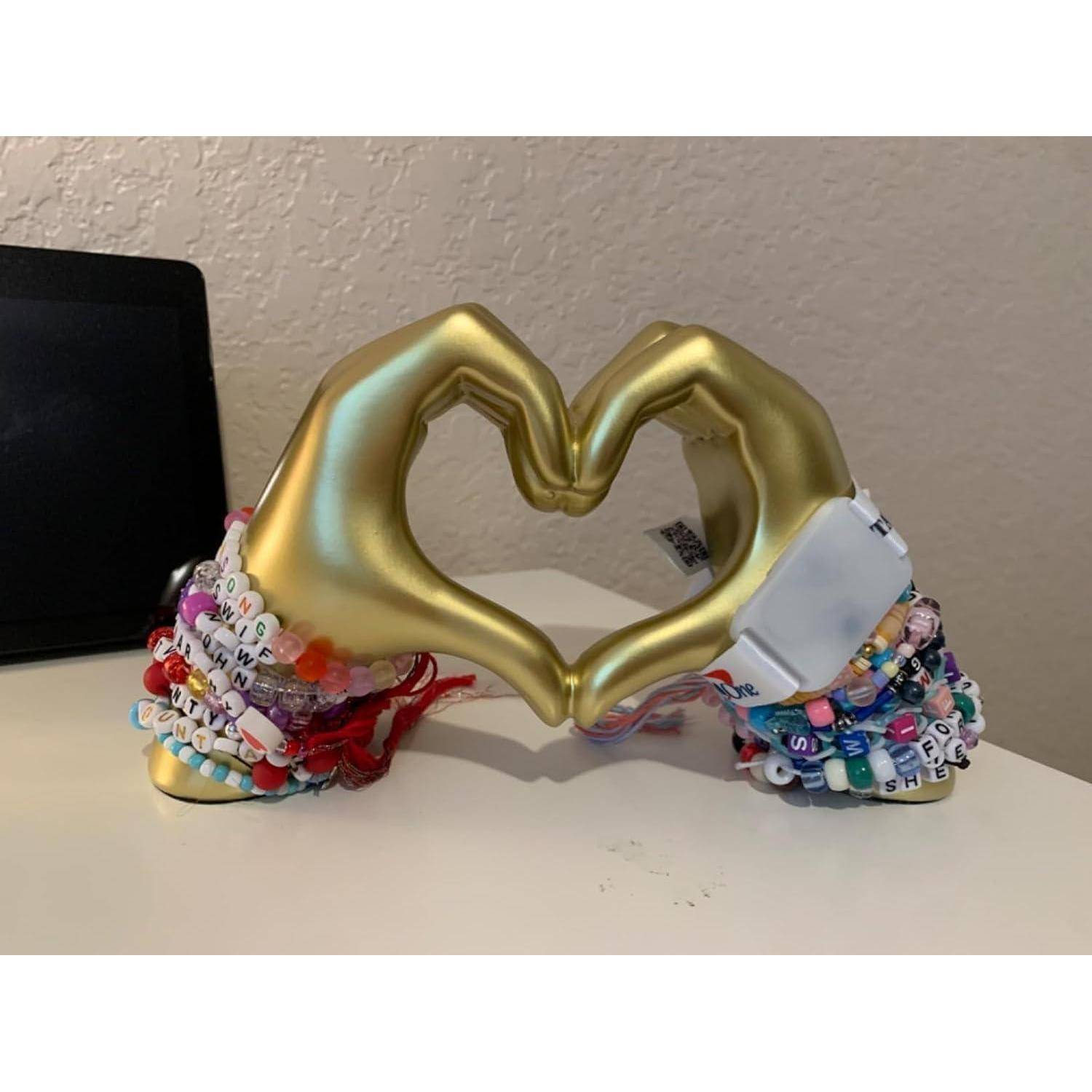 Goldhände, die eine Herzform bilden, geschmückt mit bunten Perlenarmbändern, die Liebe und Kreativität symbolisieren.