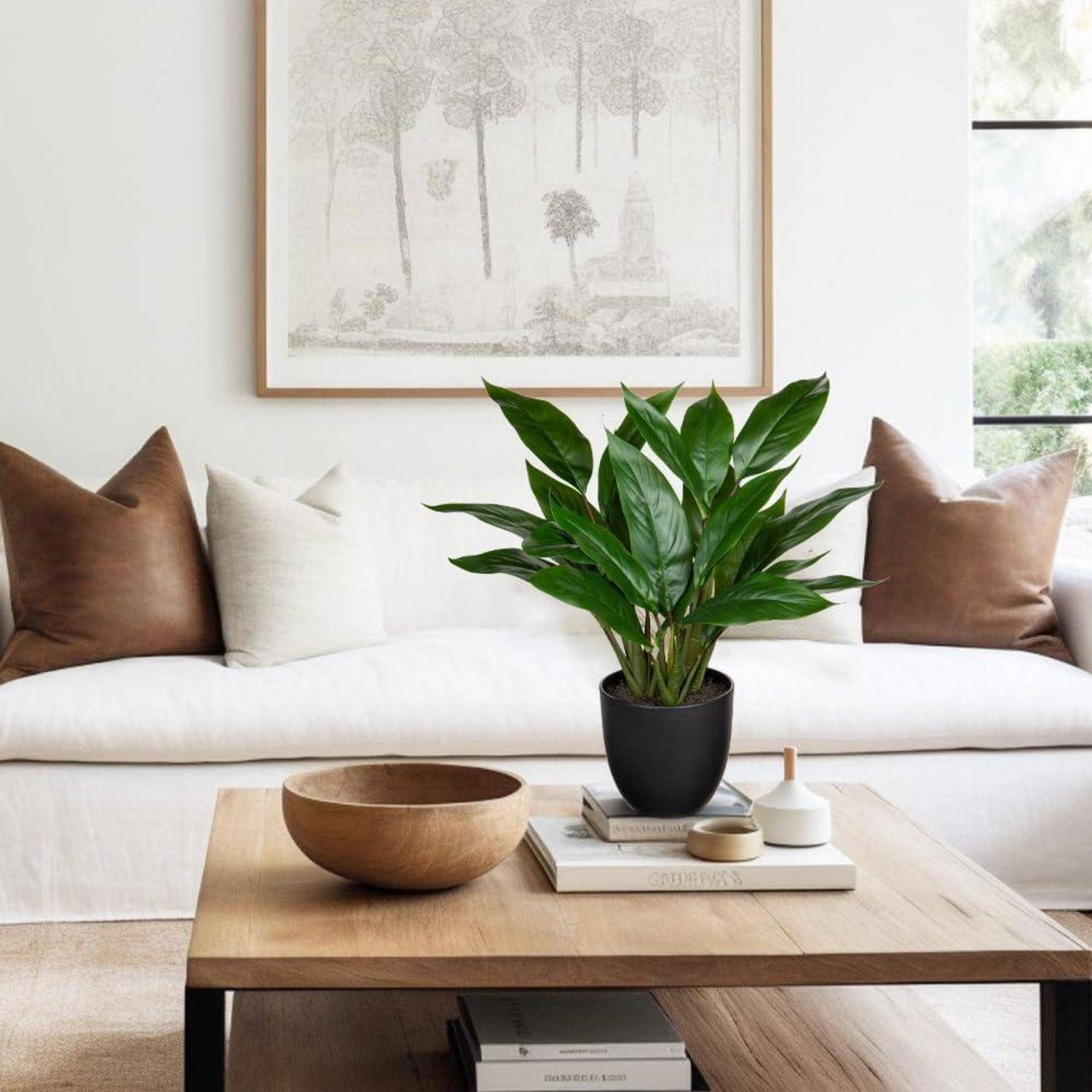Ein moderner Wohnraum mit einem weißen Sofa und braunen Kissen, einem Couchtisch mit einer Pflanze und Büchern sowie einem gerahmten Kunstwerk an der Wand.