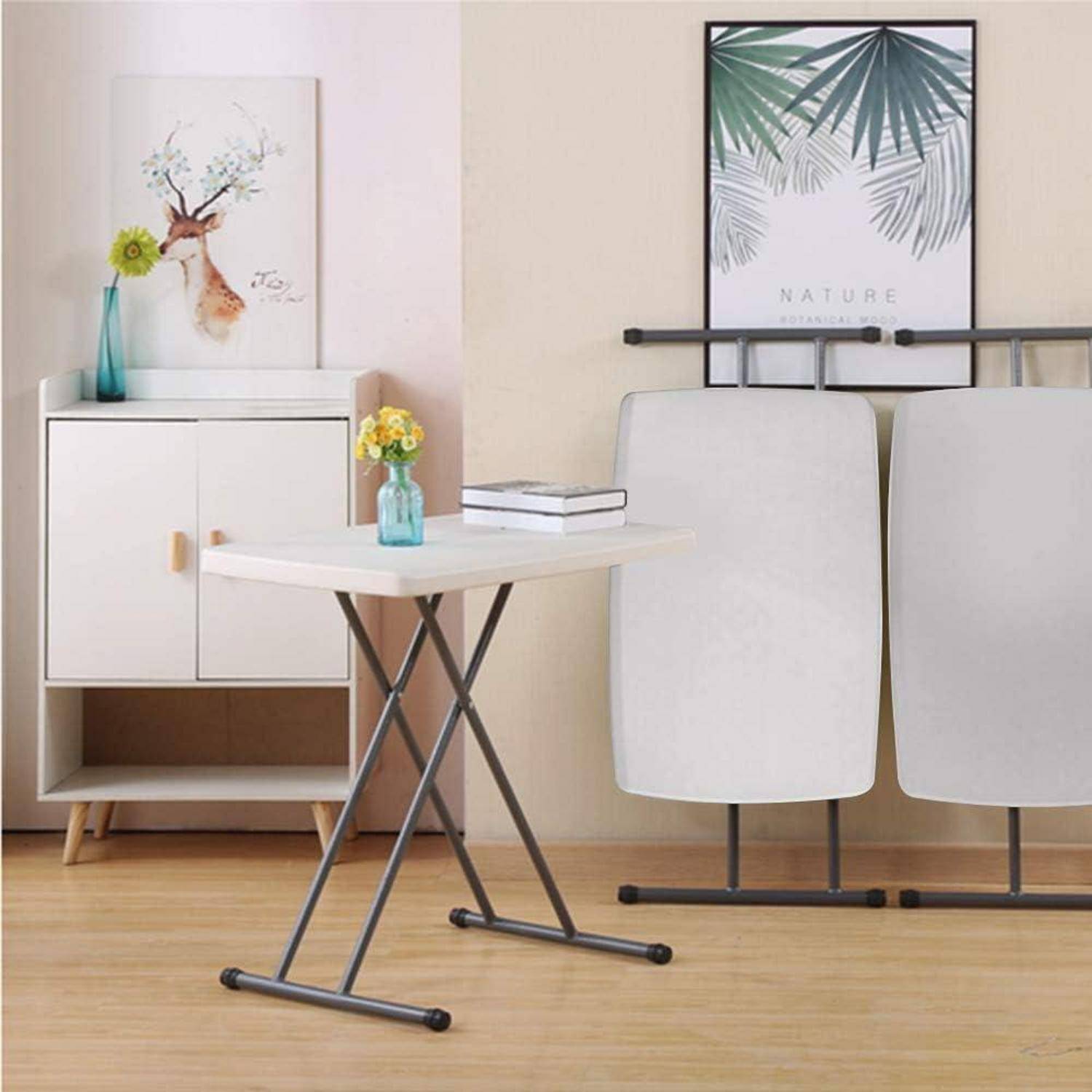 Ein minimalistisches Zimmer mit einem zusammengeklappten Tisch an der Wand, einem kleinen Schrank mit einer Hirsch-Kunstdruck, einer Vase mit gelben Blumen und Holzboden.
