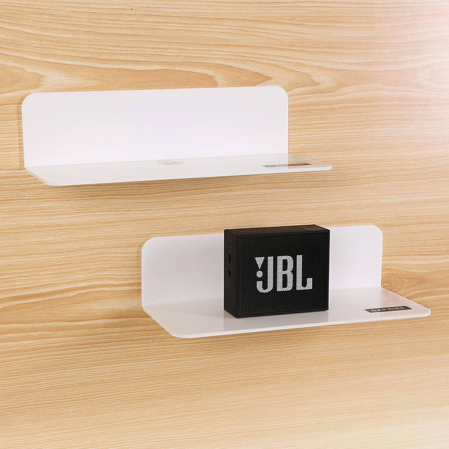 Zwei weiße wandmontierte Regale an einer hellen Holzwand. Das untere Regal trägt einen schwarzen rechteckigen Lautsprecher mit dem 'JBL' Logo.