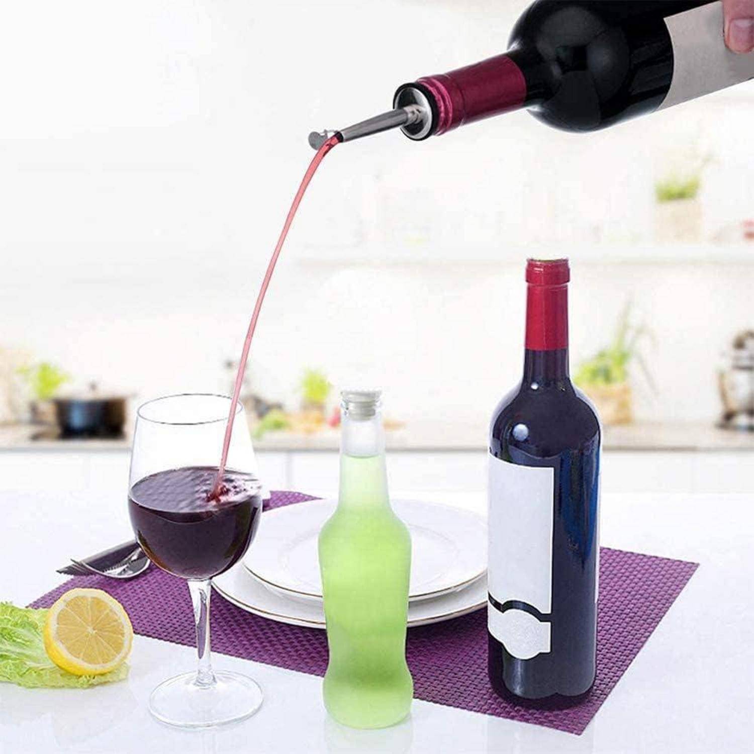 Eine Flasche Rotwein wird in ein Glas neben einer grünen Flasche eingeschenkt. Ein Zitronenschnitz und ein Salatblatt liegen auf einer lila Unterlage auf einer Küchenarbeitsplatte.