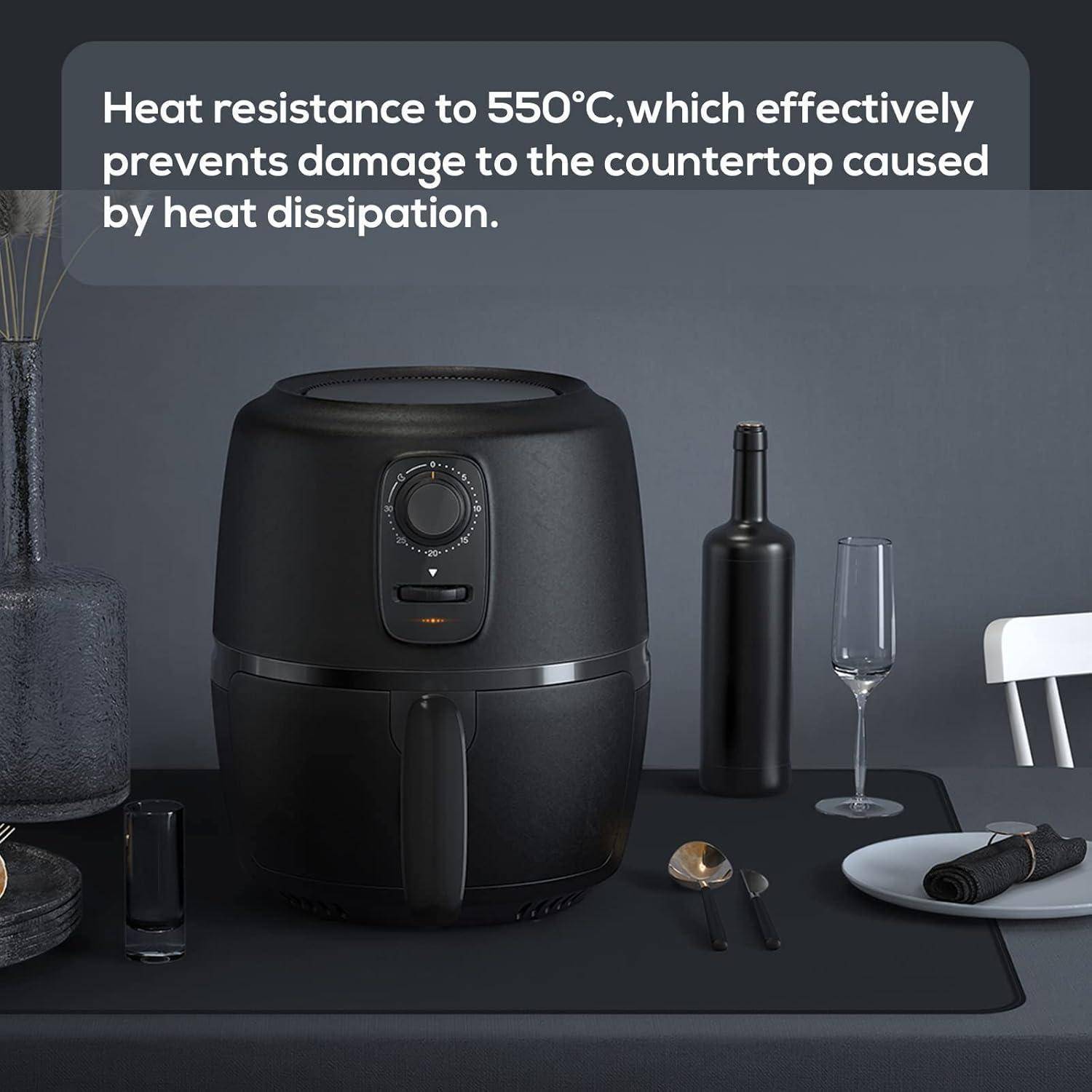 Ein schwarzer Heißluftfritteuse steht auf einem Esstisch mit Tellern, Besteck, einem Weinglas und einer Pfeffermühle. Der Text zeigt, dass er 550°C standhält.