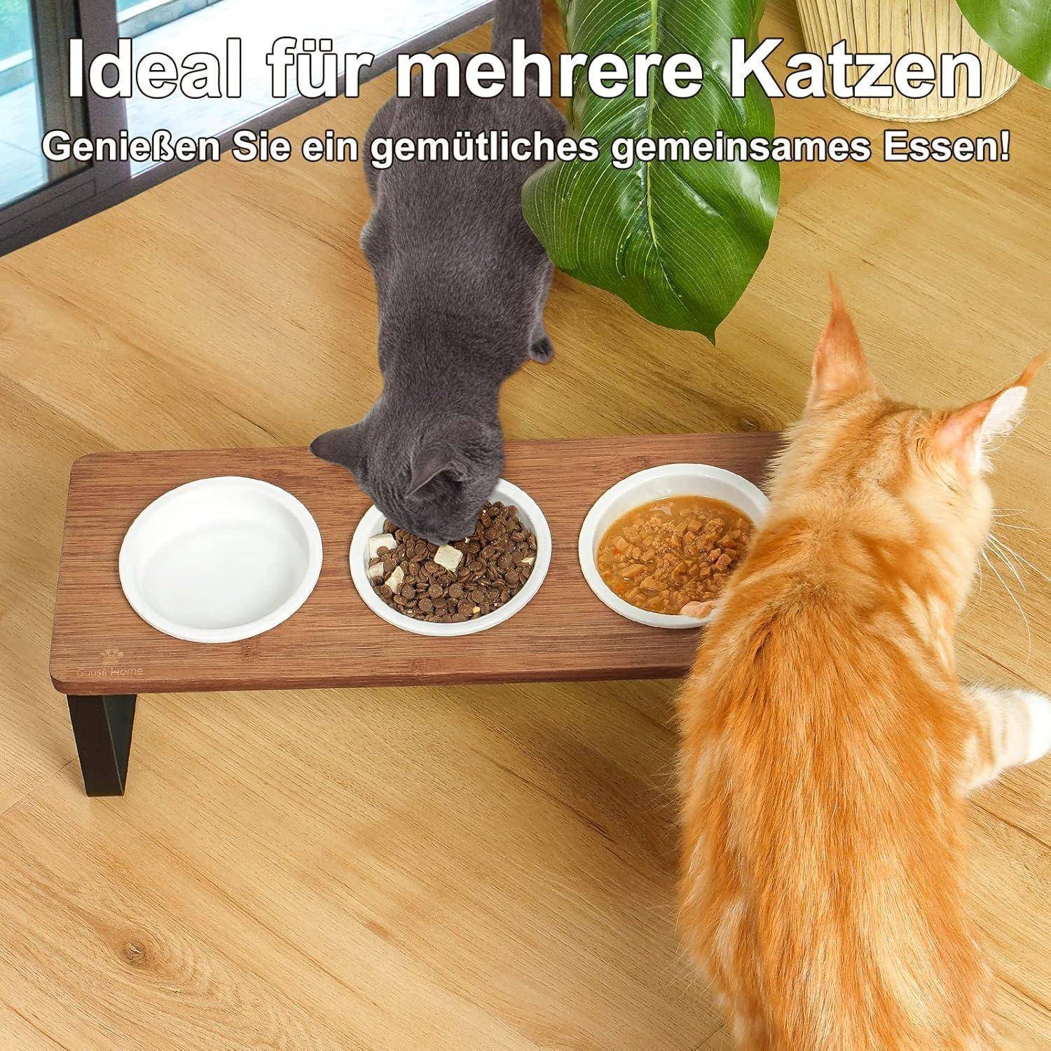 Zwei Katzen essen von einer Holz-Futterstation mit drei Schüsseln. Der Text sagt: 'Ideal für mehrere Katzen. Genießen Sie ein gemütliches gemeinsames Essen!