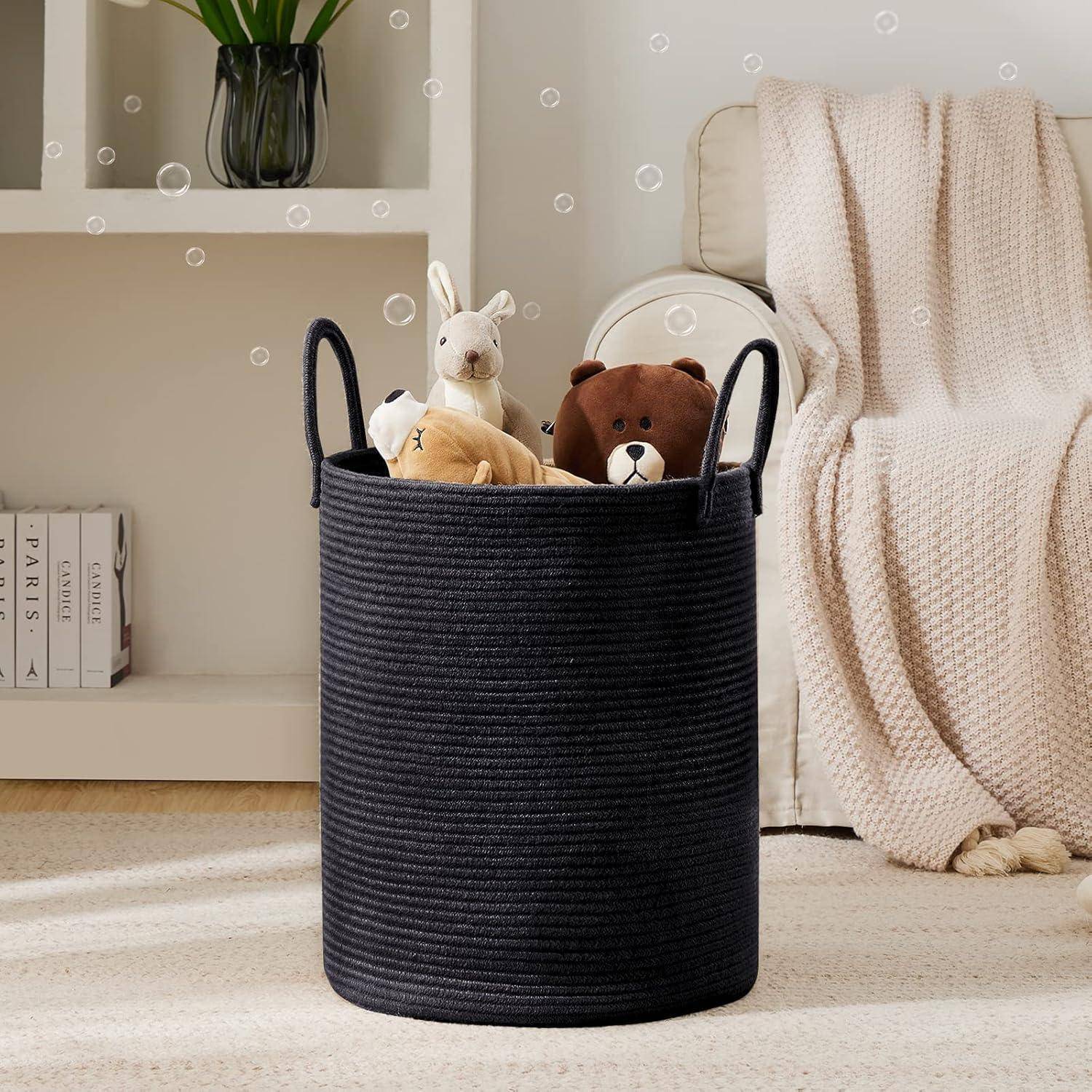 Ein schwarzer Aufbewahrungskorb enthält ein Plüschkaninchen und einen Plüschbären neben einem beigen Sofa mit einer strukturierten Decke neben einem weißen Regal und einer Vase.