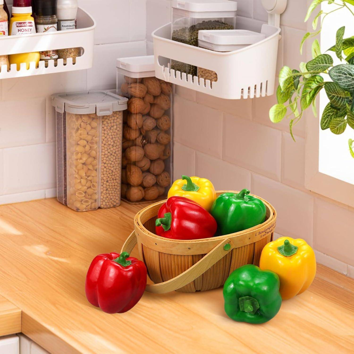 Ein Holzkorb mit roten, grünen und gelben Paprika auf einer Küchenarbeitsplatte. Regale darüber halten Gewürze, Pasta und eine Pflanze in der Nähe.