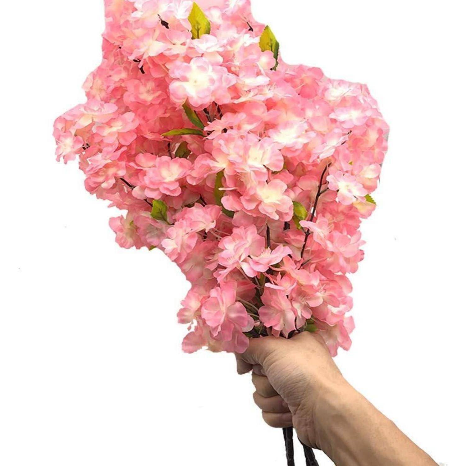Eine Hand hält einen Strauß leuchtend rosa Kirschblüten mit grünen Blättern und zeigt die zarten, vollen Blüten vor einem schlichten Hintergrund.