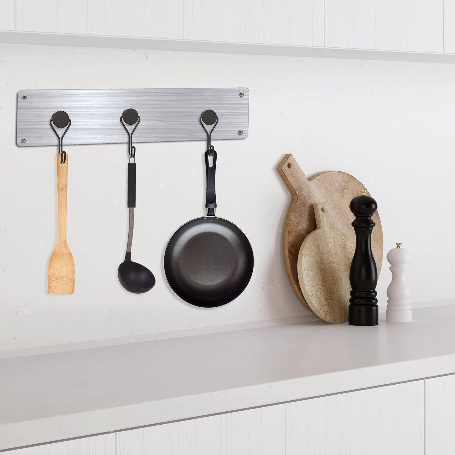 Küchenarbeitsplatte mit Utensilien: ein Holzspatel, eine Schöpfkelle und eine Pfanne hängen an Haken über Schneidebrettern, einer Pfeffermühle und einem Salzstreuer.