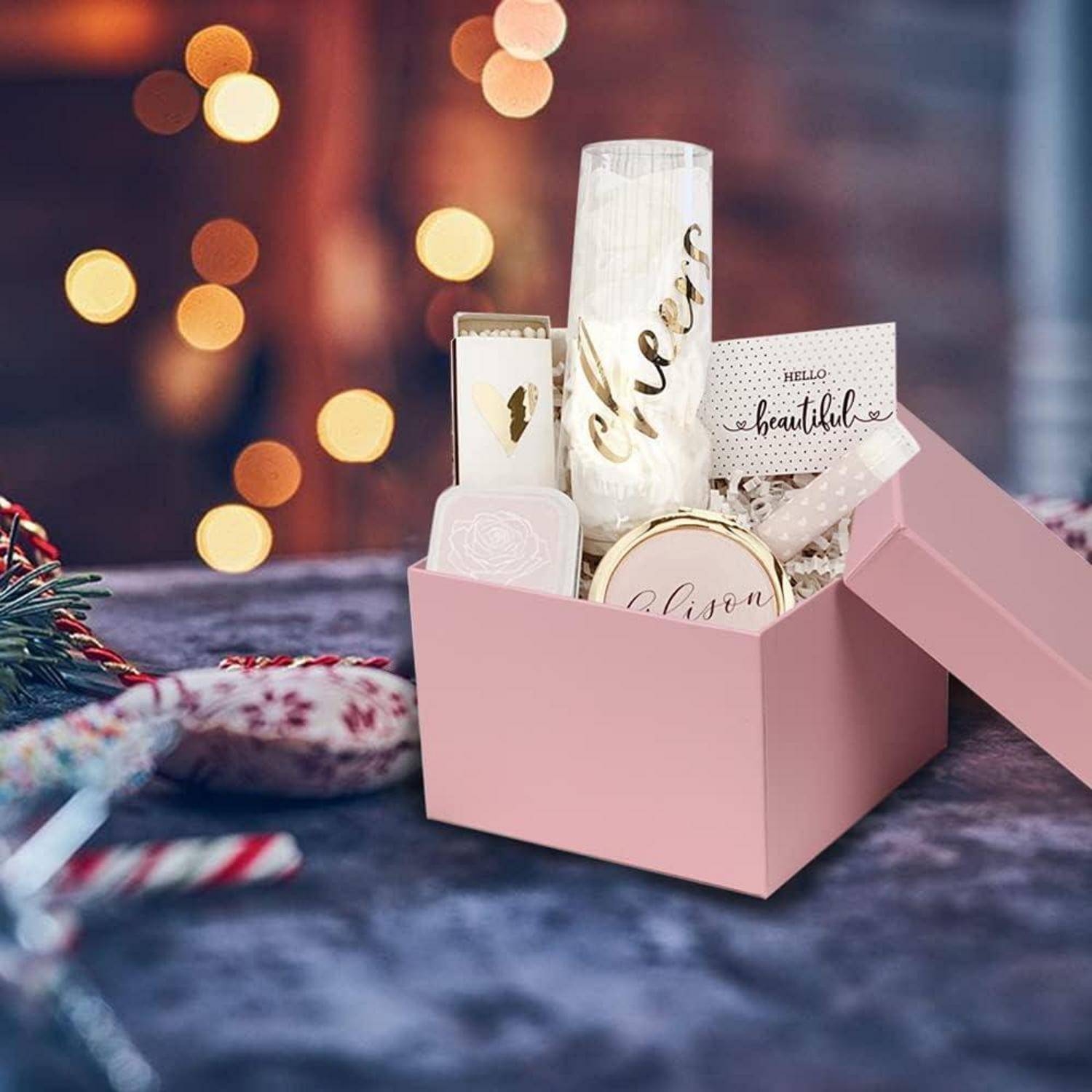 Eine rosa Geschenkbox enthält eine Kerze, eine Flasche mit der Aufschrift 