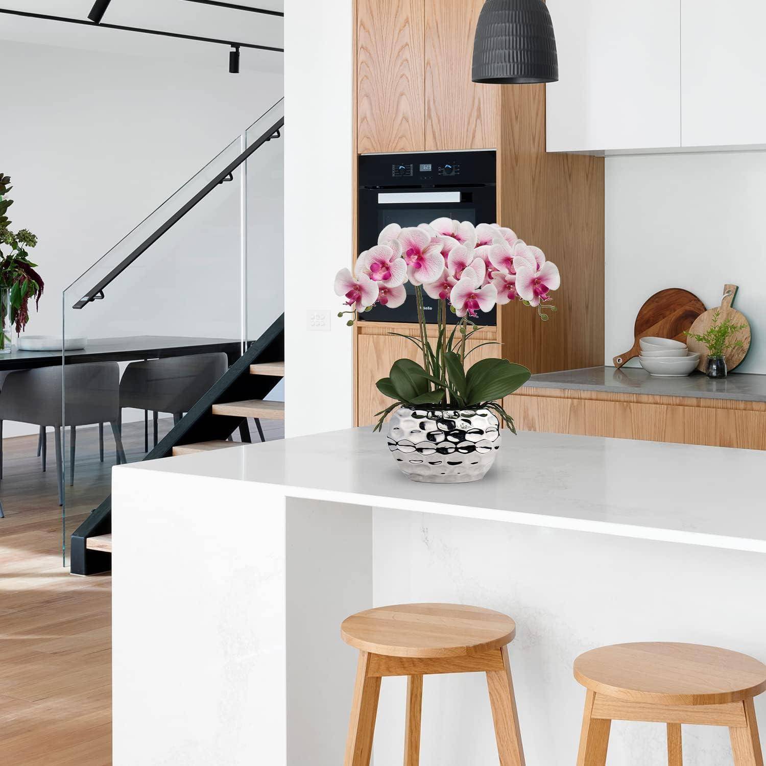 Moderne Küche mit weißer Marmortheke, Holzhockern und Edelstahlgeräten. Rosa Orchideen in einem silbernen Topf verschönern die Dekoration.