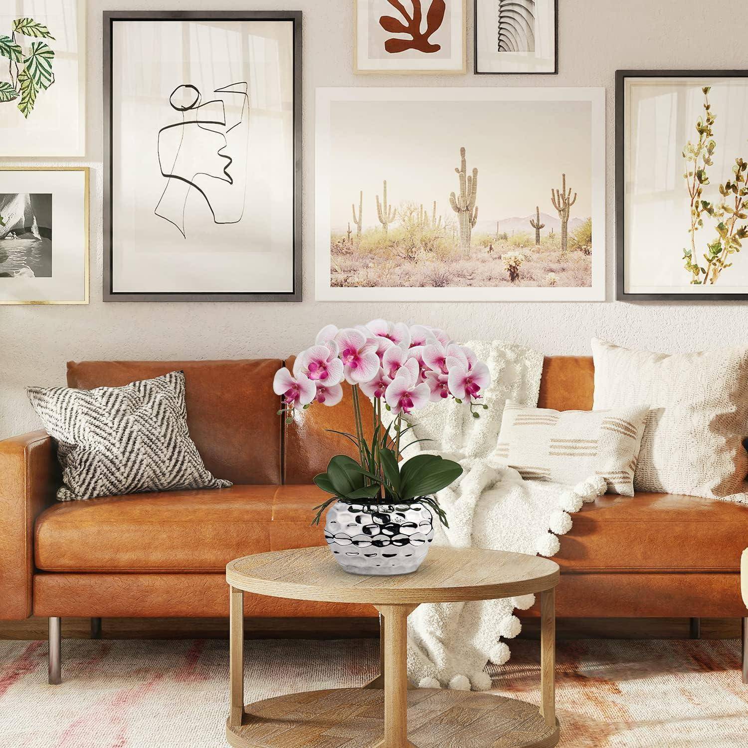 Ein gemütliches Wohnzimmer mit einem braunen Ledersofa, gemusterten Kissen, einem kleinen runden Tisch mit rosa Orchideen in einer Vase und gerahmten Kunstwerken an der Wand.