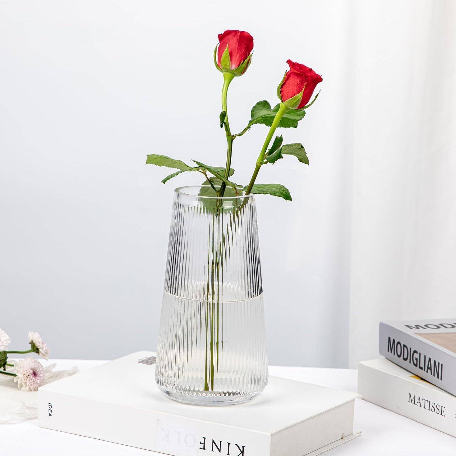 Eine klare Vase mit zwei roten Rosen steht auf einem weißen Buch mit dem Titel 