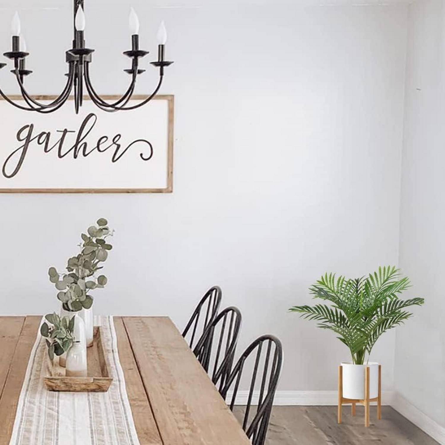 Ein Esszimmer mit einem Holztisch, schwarzen Stühlen und einem schwarzen Kronleuchter. Ein Schild an der Wand liest 'zusammenkommen'. Pflanzen bringen Grün.