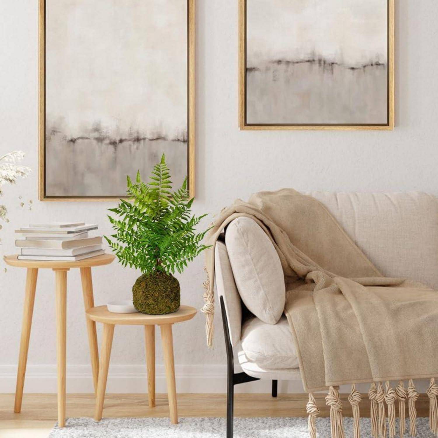 Ein gemütliches Wohnzimmer zeigt eine beige Couch mit einer weichen Decke, einen Holz-Beistelltisch mit einer Farnpflanze in einem Topf und zwei abstrakte Gemälde.