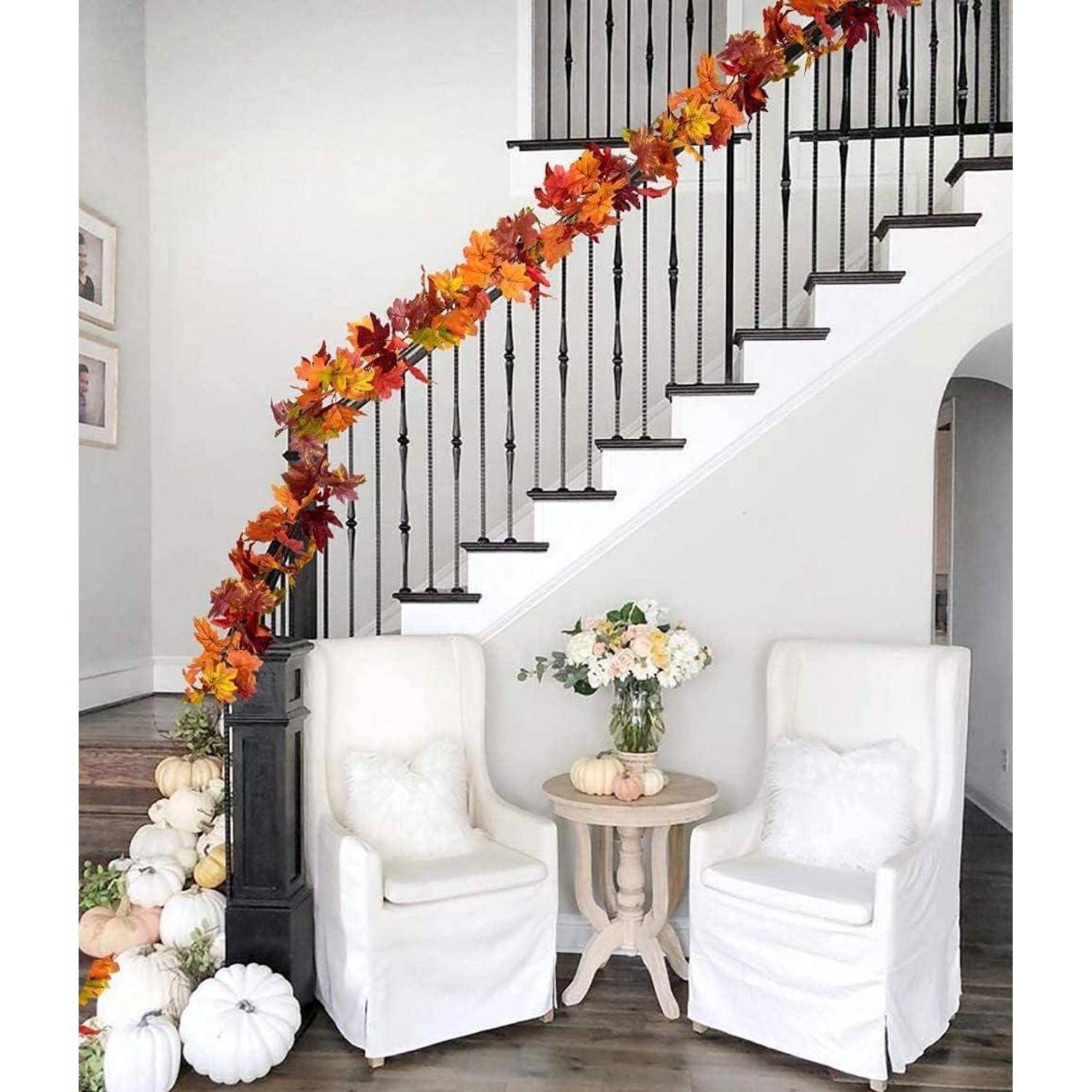 Eine Treppe mit einer Girlande aus Herbstblättern, weißen Kürbissen auf den Stufen und zwei weißen Stühlen mit einem kleinen Tisch und einer Blumenarrangement in der Nähe.