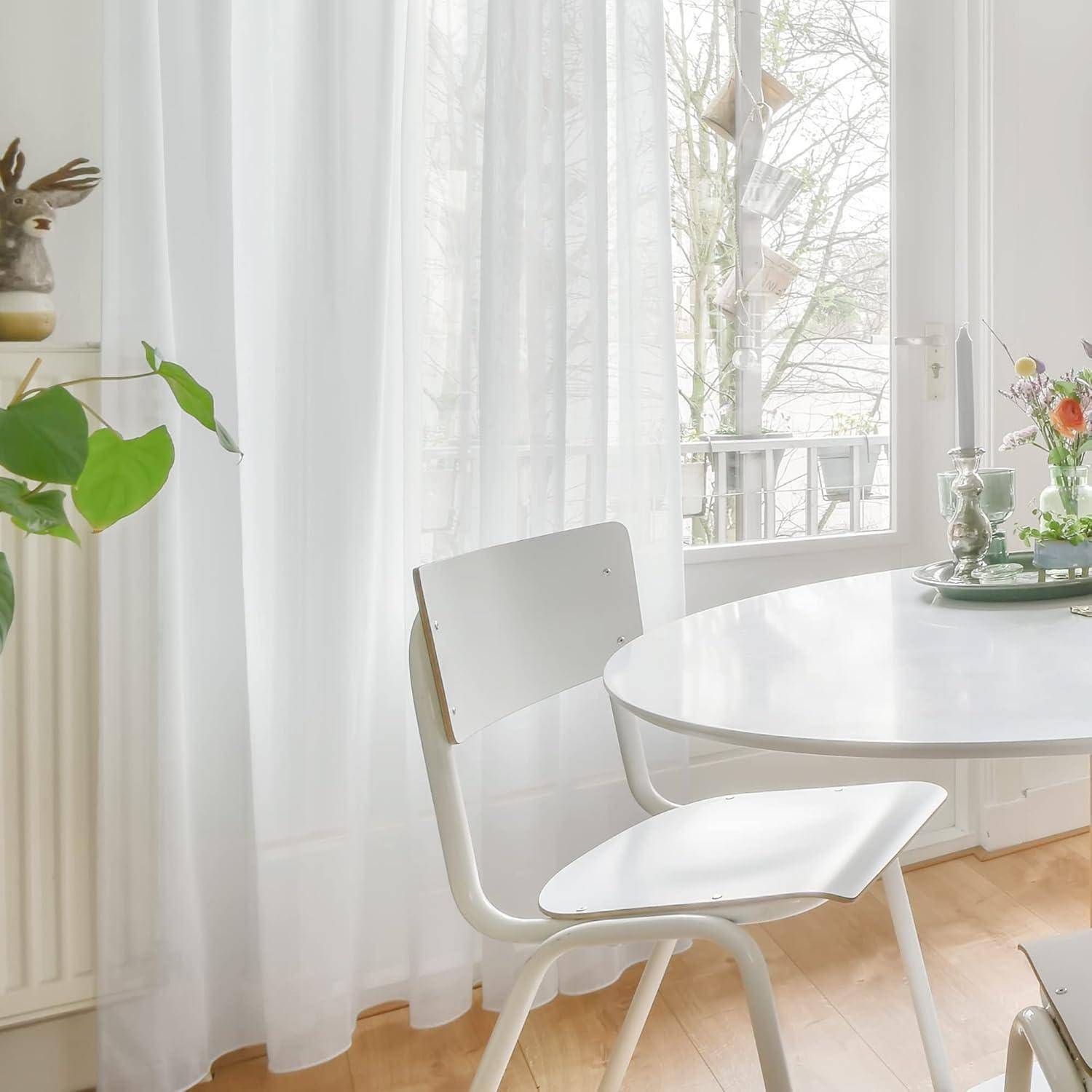 Ein heller Essbereich mit einem runden Tisch, einem weißen Stuhl und einer Pflanze in der Nähe eines Fensters. Natürliches Licht durchflutet den Raum und schafft eine ruhige Atmosphäre.
