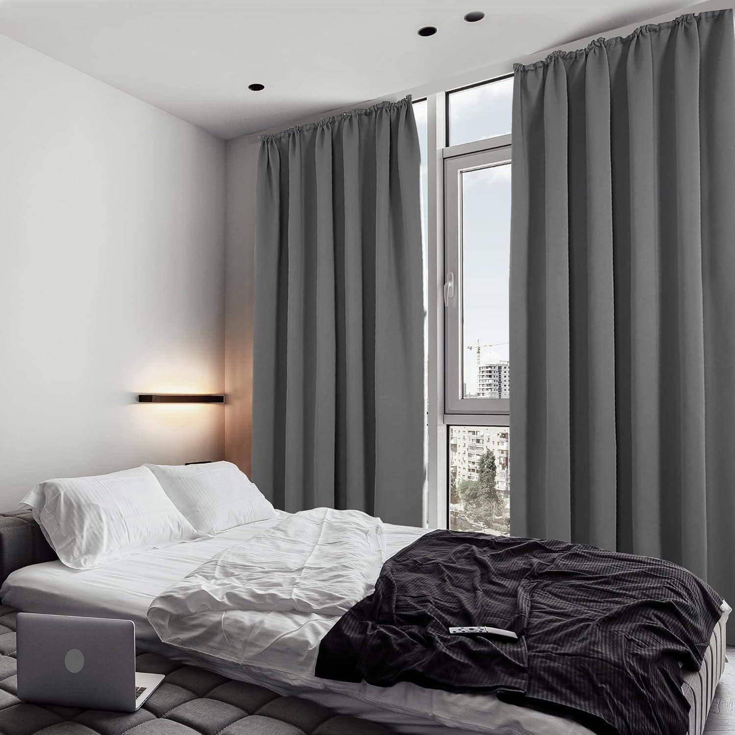 Ein modernes Schlafzimmer mit einem großen Bett, das mit weißer und dunkler Bettwäsche ausgestattet ist, neben einem hohen Fenster mit geschlossenen grauen Gardinen, das einen Blick auf die Stadtlandschaft bietet.