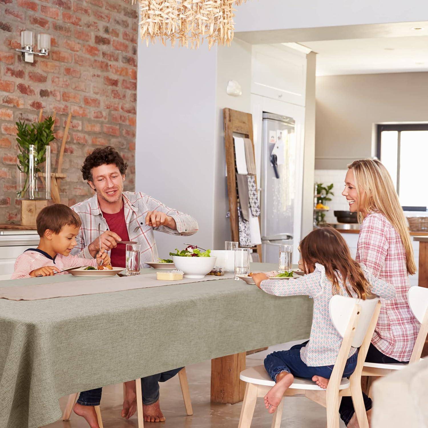 Eine Familie sitzt zusammen an einem Tisch, wobei ein Mann Essen serviert, zwei Kinder ungeduldig warten und eine Frau lächelt. Der Raum ist hell und gemütlich.