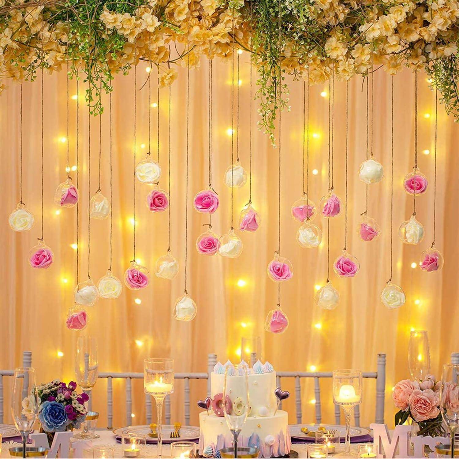 Ein wunderschön dekorierter Hochzeitstisch mit hängenden Rosen, leuchtenden Lichterketten und einer weißen Torte, umgeben von Kerzen und Blumenarrangements.