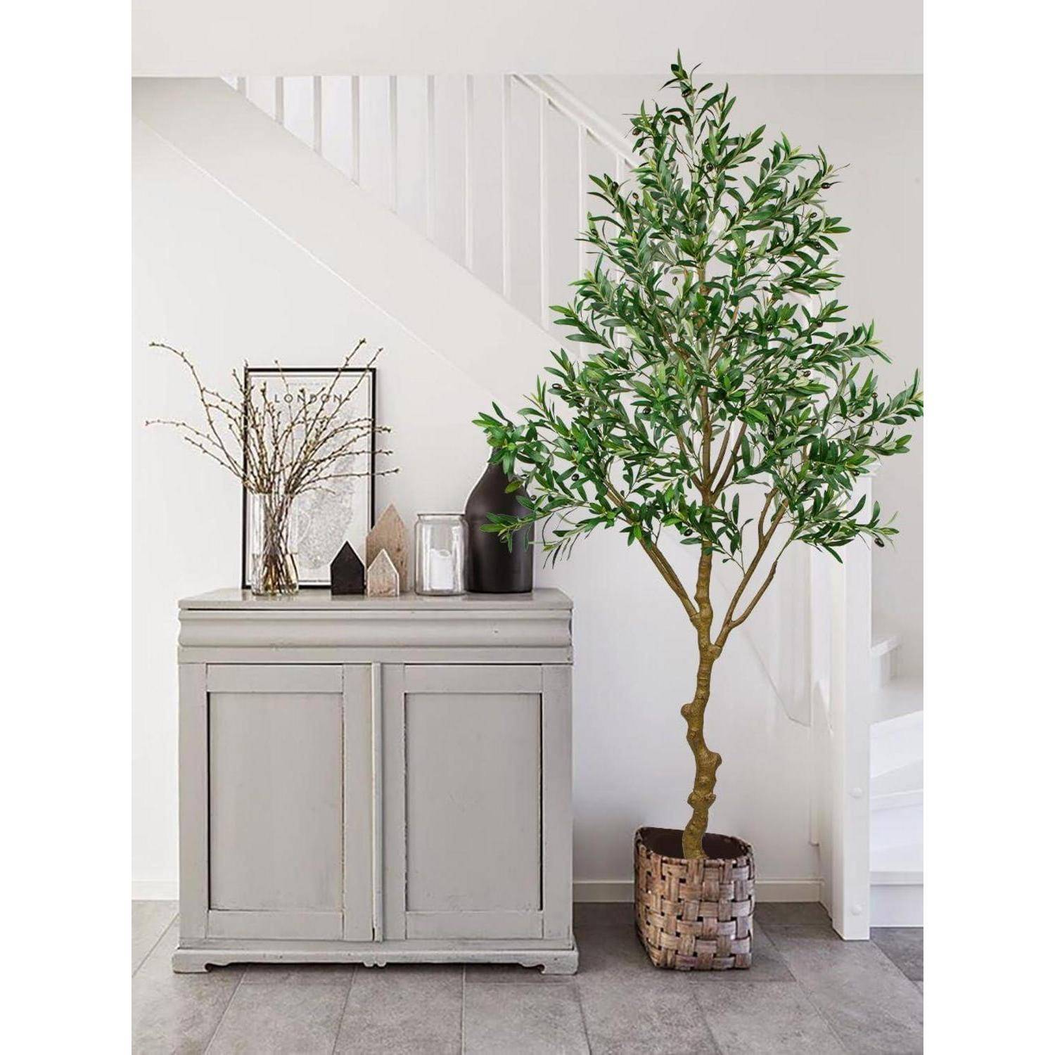 Ein Topfbaum mit grünen Blättern steht neben einem hellgrauen Schrank, der mit Vasen und Zweigen bestückt ist, direkt neben einer weißen Treppe in einem minimalistischen Raum.