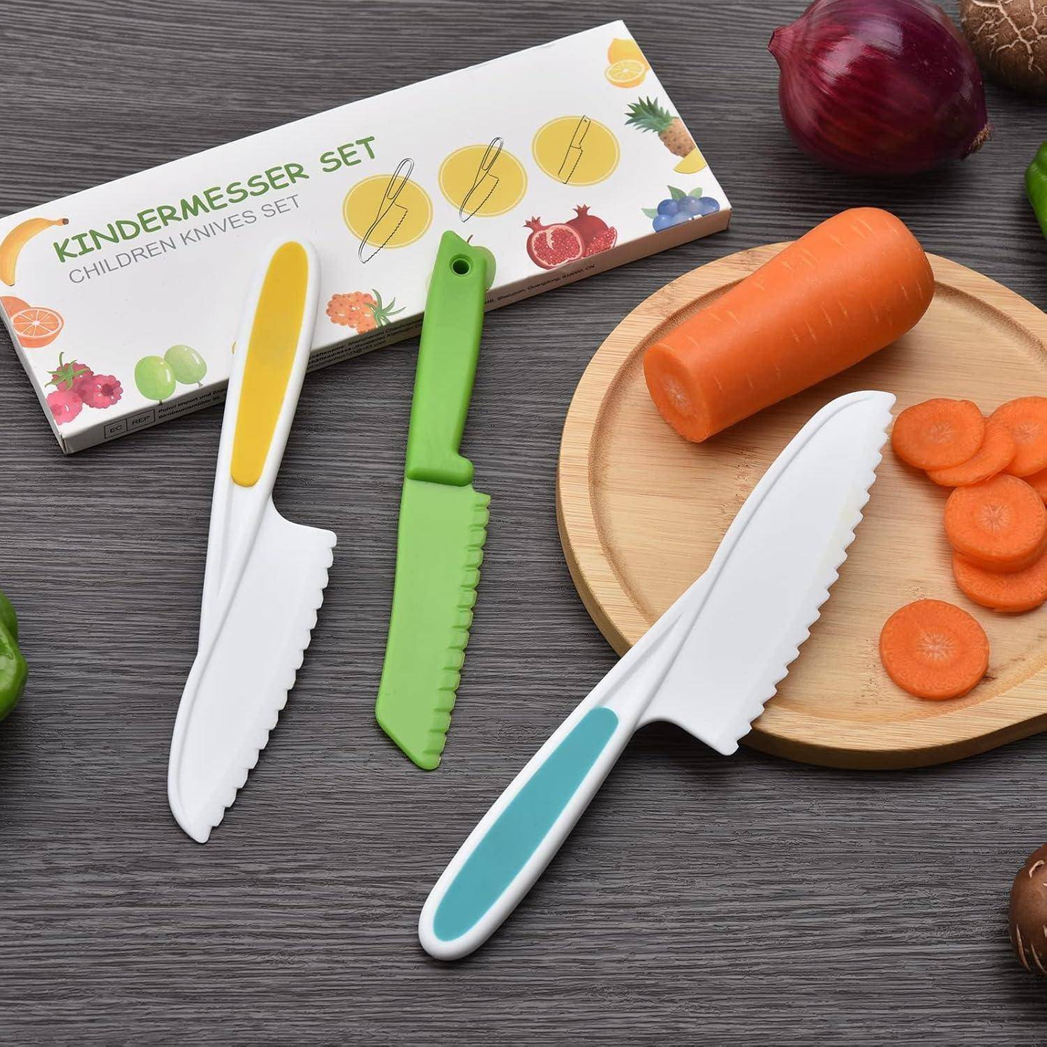 Ein Set aus drei kindersicheren Messern und einer geschnittenen Karotte auf einem Schneidebrett. Eine Schachtel mit der Aufschrift 