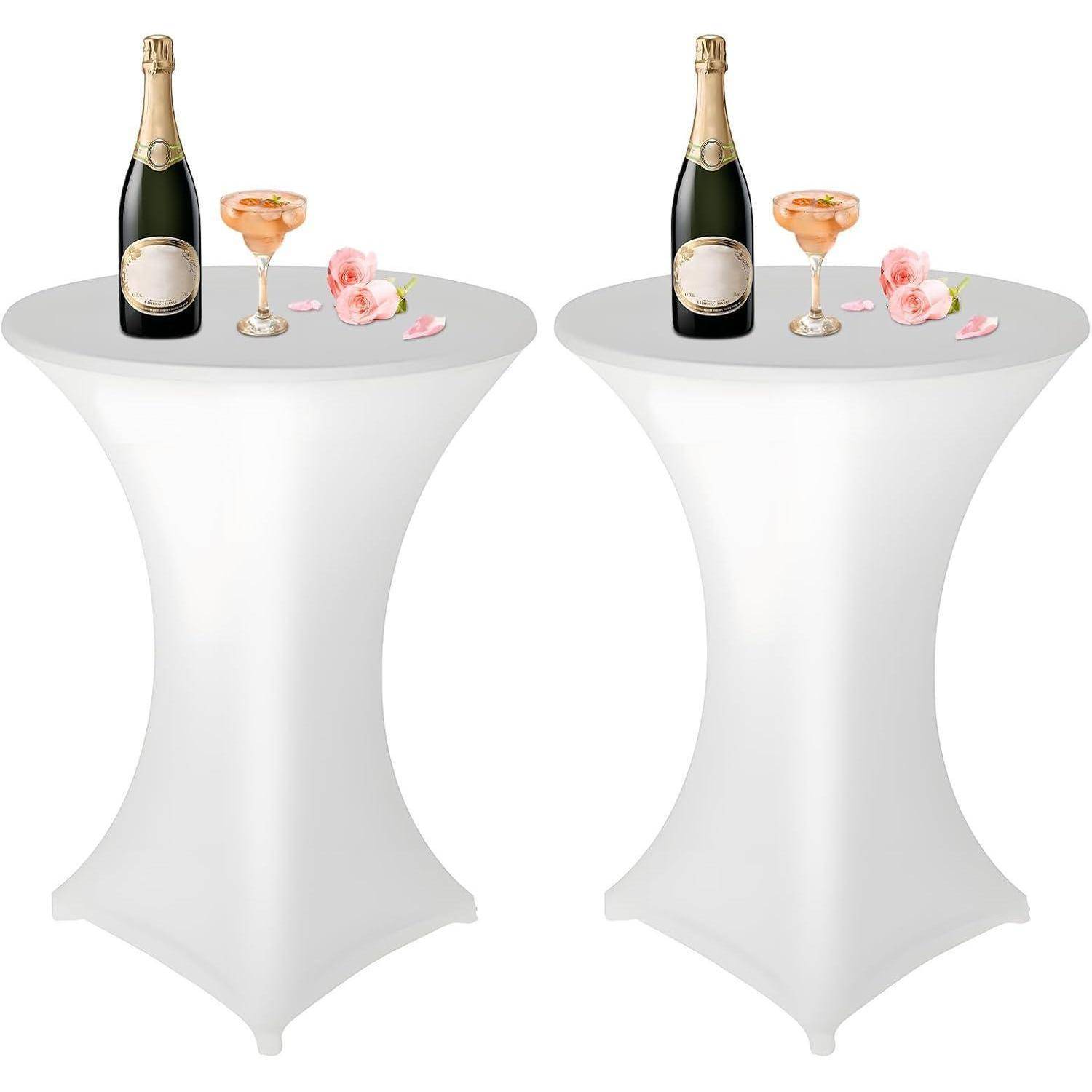 Zwei hohe runde Tische mit weißen Überwürfen, auf denen jeweils eine Flasche Champagner, zwei gefüllte Gläser und rosa Blumen stehen.