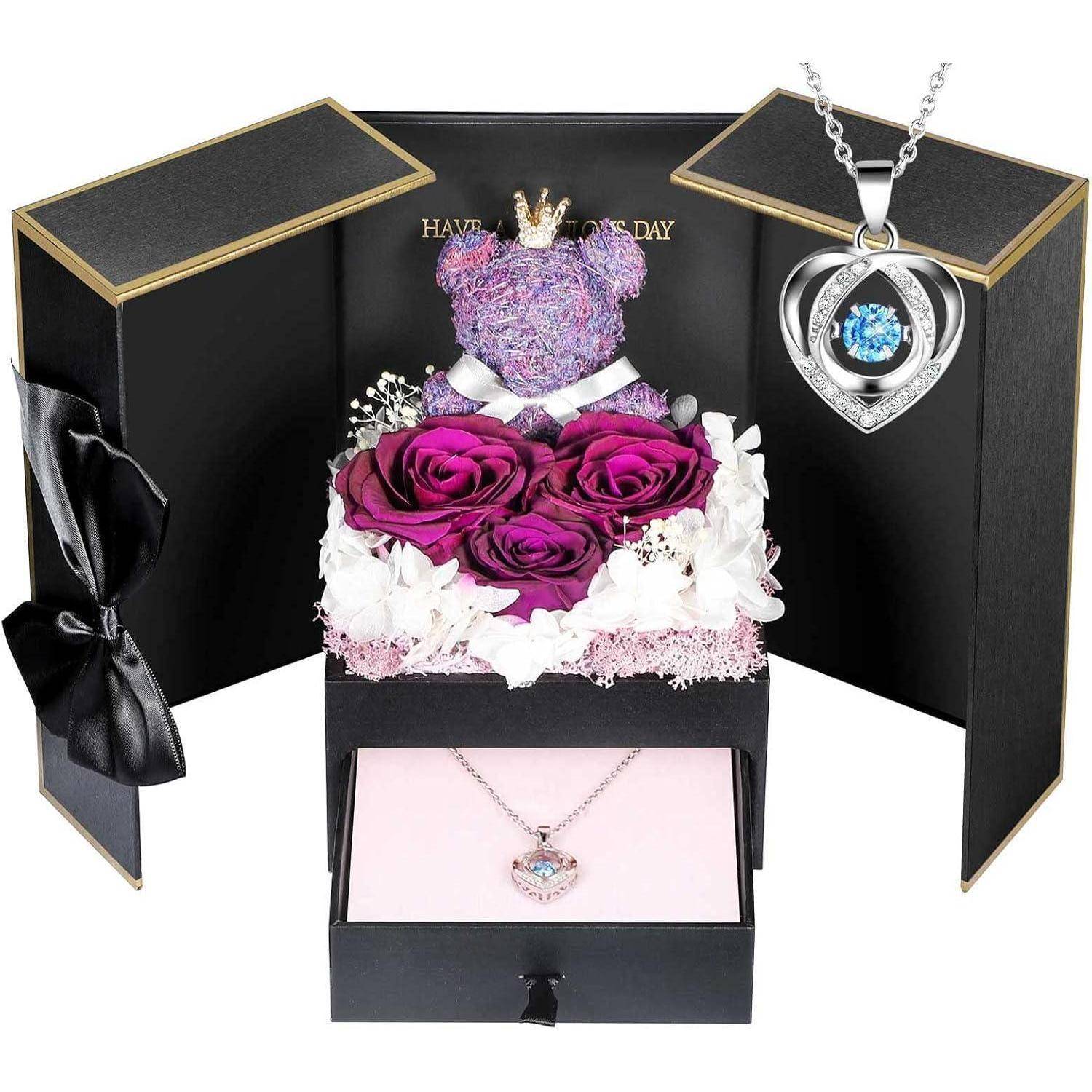 Geschenkset mit einer silbernen Halskette, lila Rosen und weißen Blumen in einer Schachtel. Der Deckel trägt die Aufschrift 