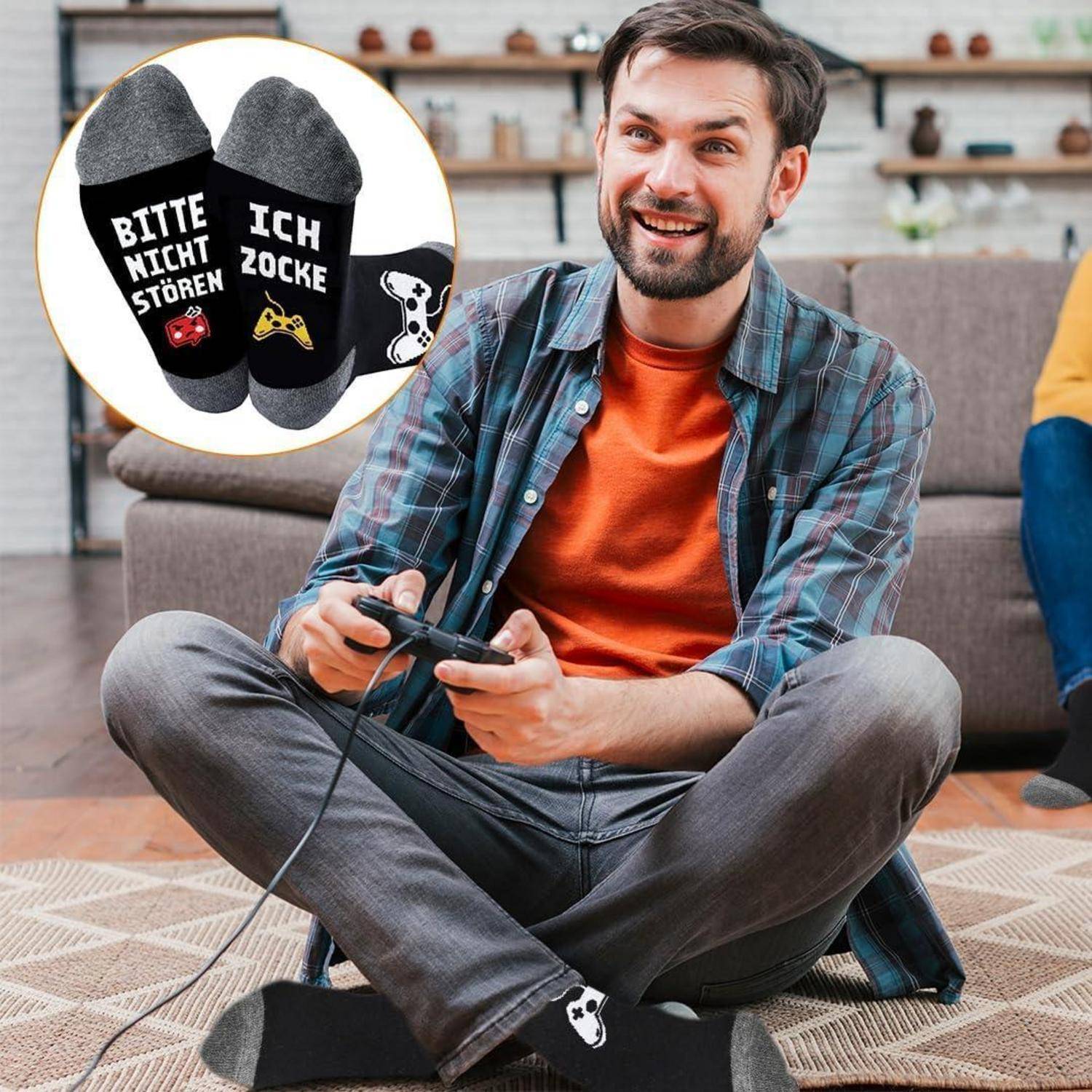 Ein lächelnder Mann sitzt auf dem Boden und hält einen Gamecontroller. Seine Socken tragen die Aufschrift ‚Bitte nicht stören, ich zocke'.