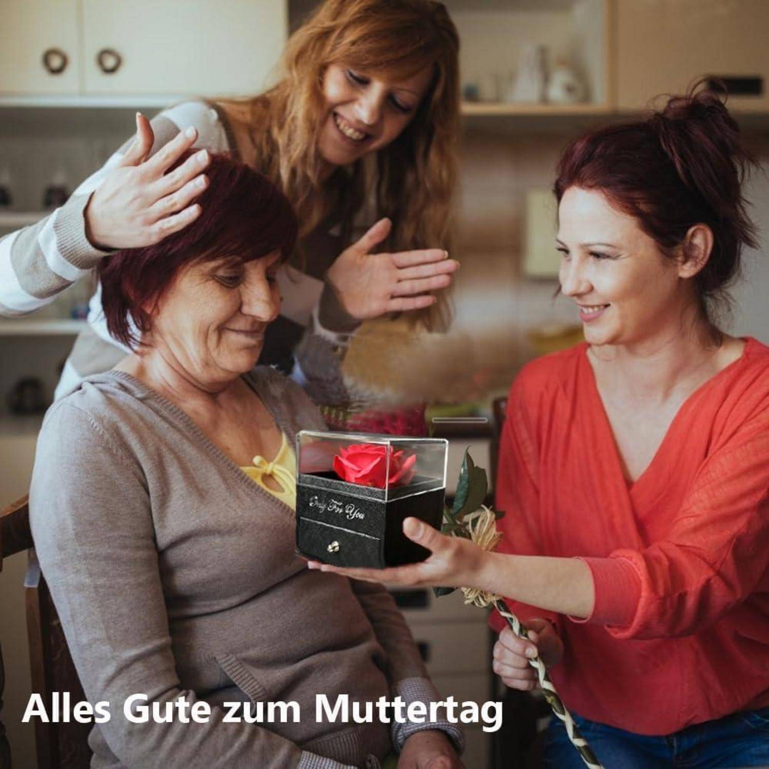 Drei Menschen versammeln sich in einem gemütlichen Raum. Eine Frau überreicht einer älteren Frau ein Geschenk und eine rote Rose und feiert so den Muttertag.