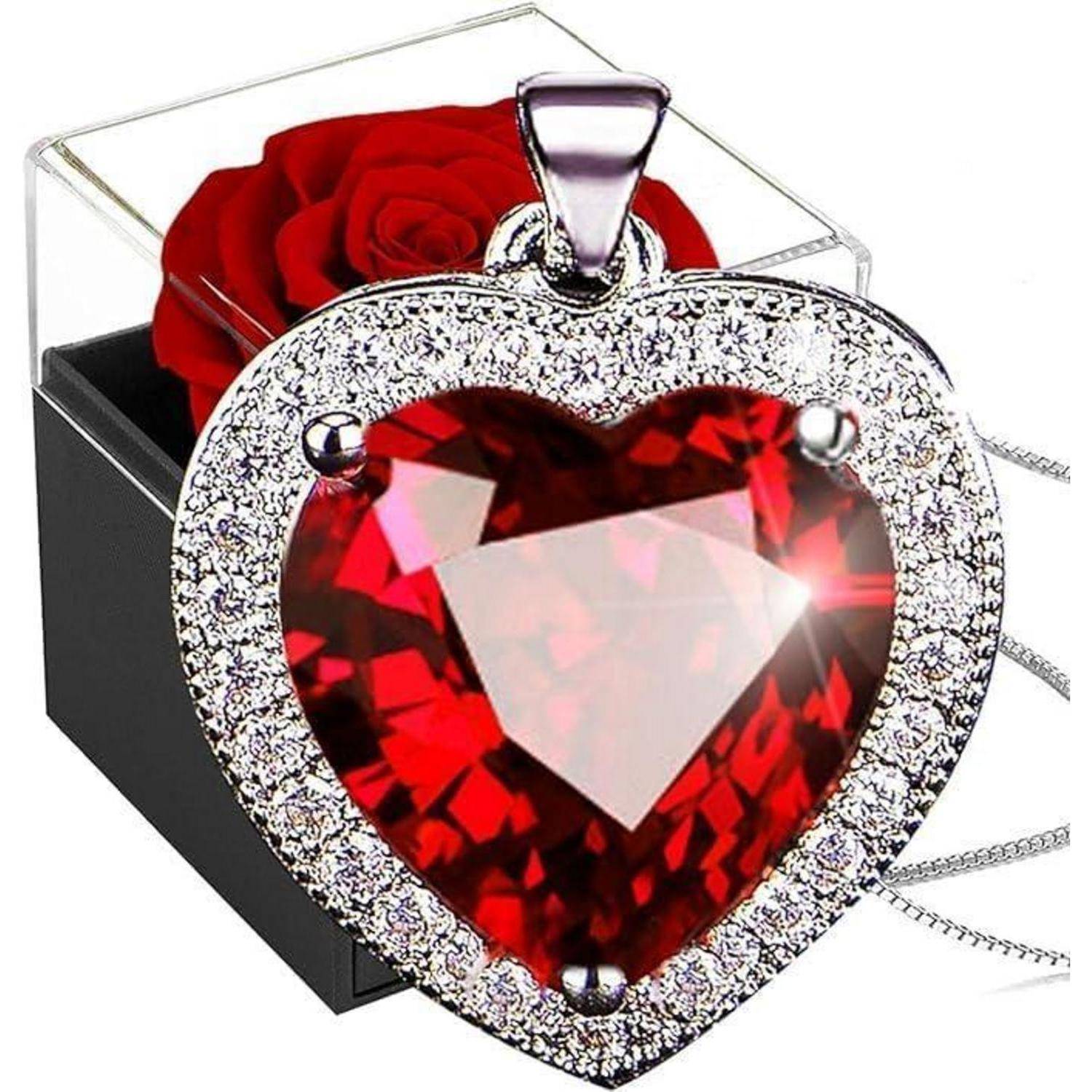 Eine herzförmige rote Edelsteinkette mit einem diamantenbesetzten Rand wird vor einer schwarzen Box mit einer roten Rose präsentiert.
