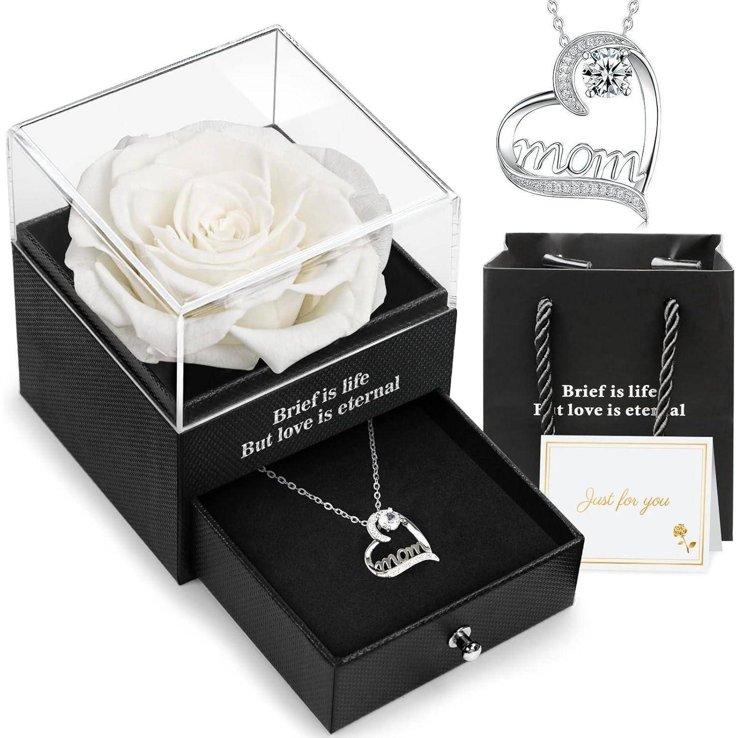 Eine weiße Rose in einer durchsichtigen Box mit einer Herzkette neben einem Anhänger mit der Aufschrift 