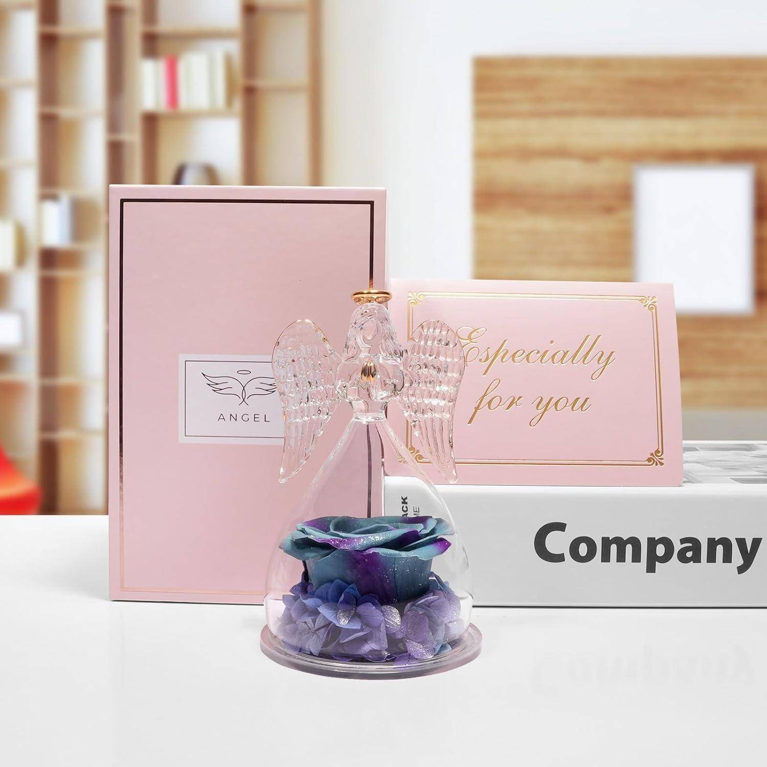 Eine Glasengelfigur auf einem lila und blauen Blumenuntergrund steht vor einer rosa Schachtel mit der Aufschrift „Besonders für dich