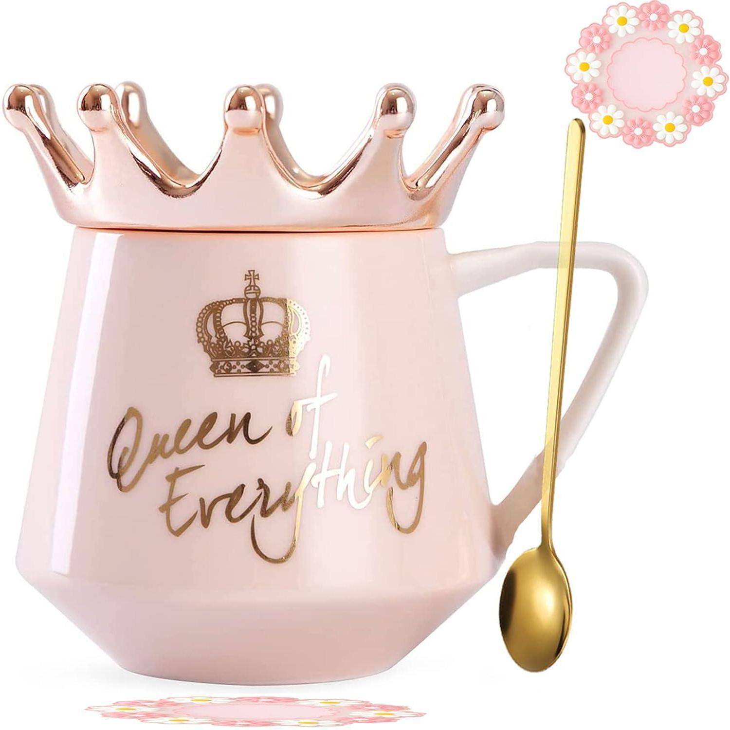 Rosa Becher mit einem kronenförmigen Deckel, auf dem in Gold 'Queen of Everything' geschrieben steht. Mit einem goldenen Löffel und einem floralen Untersetzer-Design.