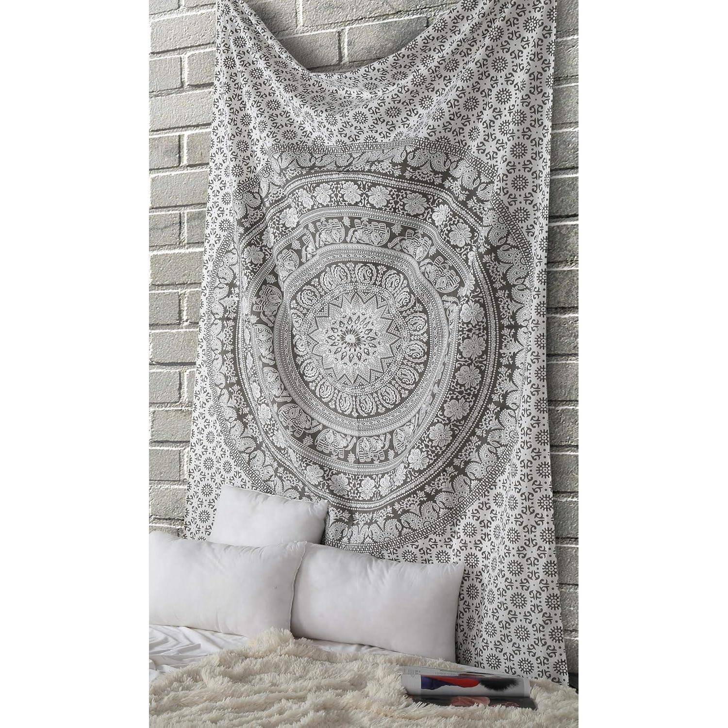 Ein detaillierter Wandteppich mit komplexen kreisförmigen Mustern hängt an einer Ziegelwand über einem Bett mit weißen Kissen und einer strukturierten Decke.