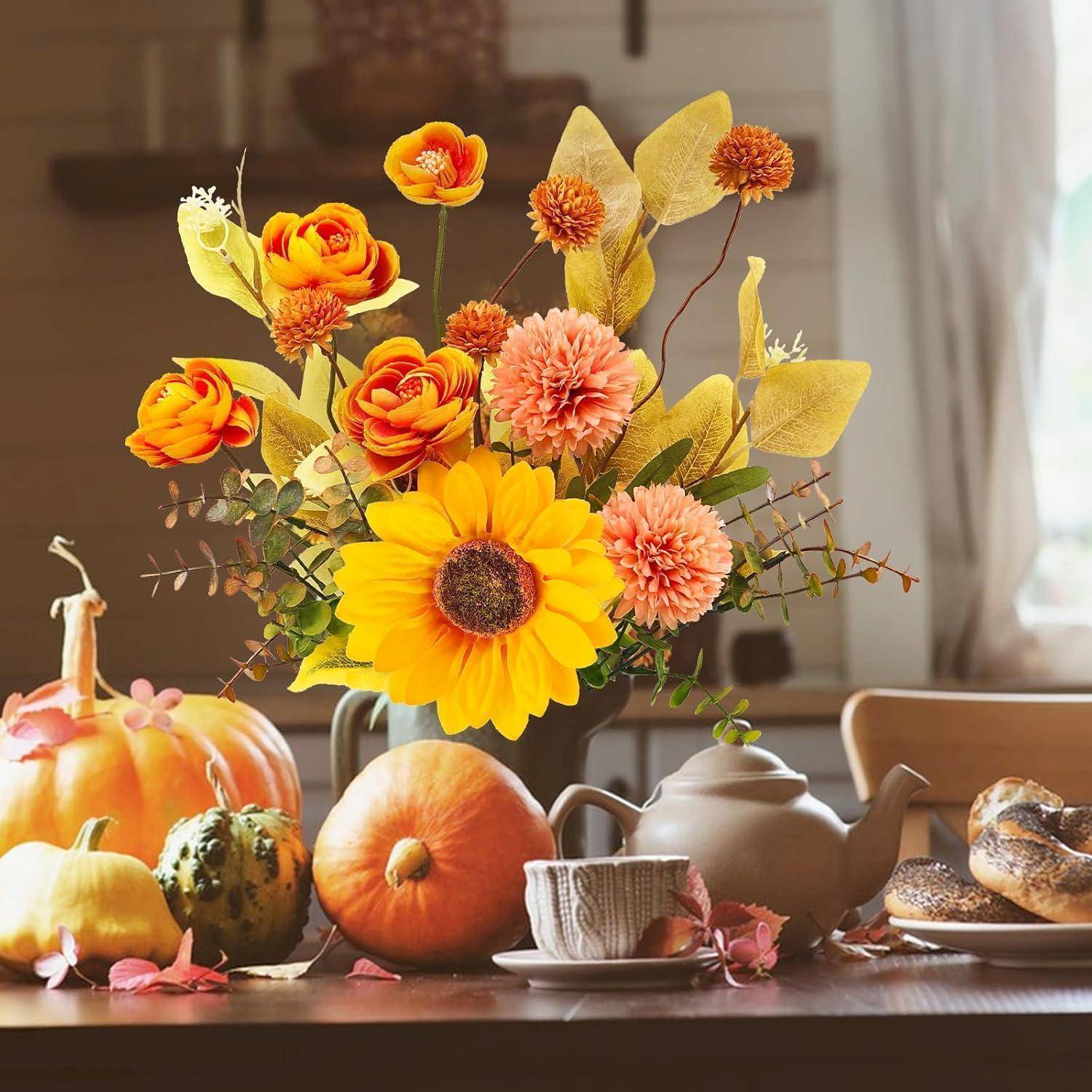 Ein lebendiges Herbst-Mittelstück mit Sonnenblumen, orange und rosa Blumen, umgeben von Kürbissen und Zierkürbissen auf einem Holztisch.