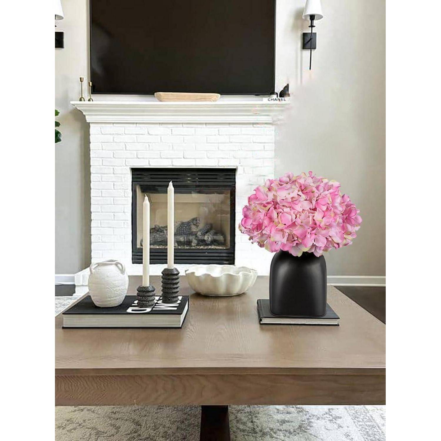 Ein Wohnzimmer mit einem weißen BacksteinKamin, einem Fernseher darüber und einem Holzcouchtisch. Auf dem Tisch stehen rosa Blumen, Kerzen und dekorative Gegenstände.