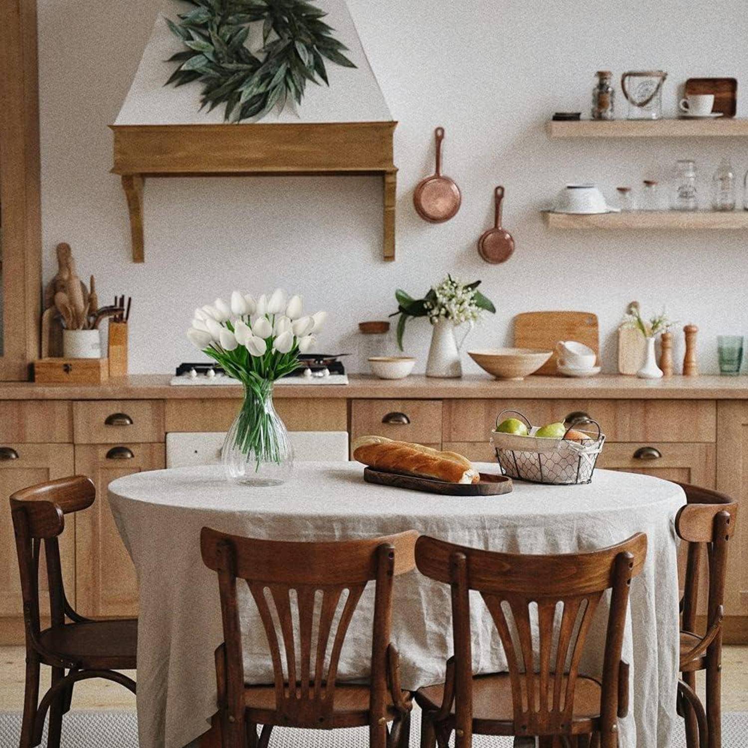 Eine rustikale Küche mit Holzschränken und -regalen, die einen für eine Mahlzeit gedeckten Tisch mit Blumen, Brot und Obst in einer warmen, einladenden Atmosphäre zeigt.