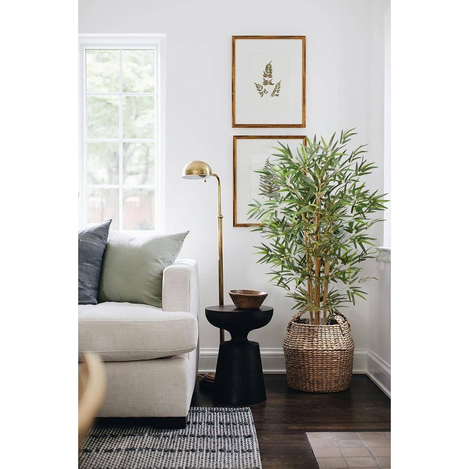 Eine gemütliche Ecke im Wohnzimmer mit einem beigen Sofa, grünem Kissen, schwarzem rundem Beistelltisch, Messinglampe, Topfpflanze und gerahmter botanischer Kunst.